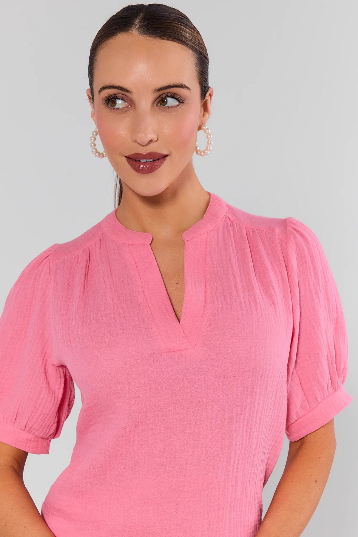 Woman wearing a pink blouse with short sleeves against a plain background