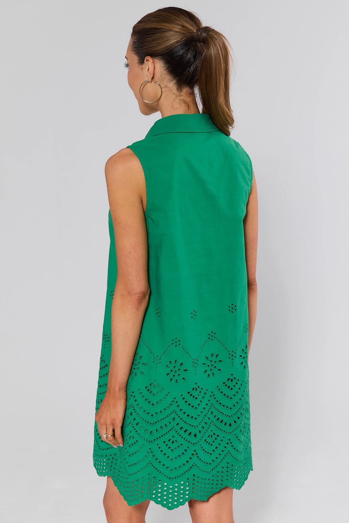 Woman standing wearing a green sleeveless dress with intricate lace detailing on a plain background