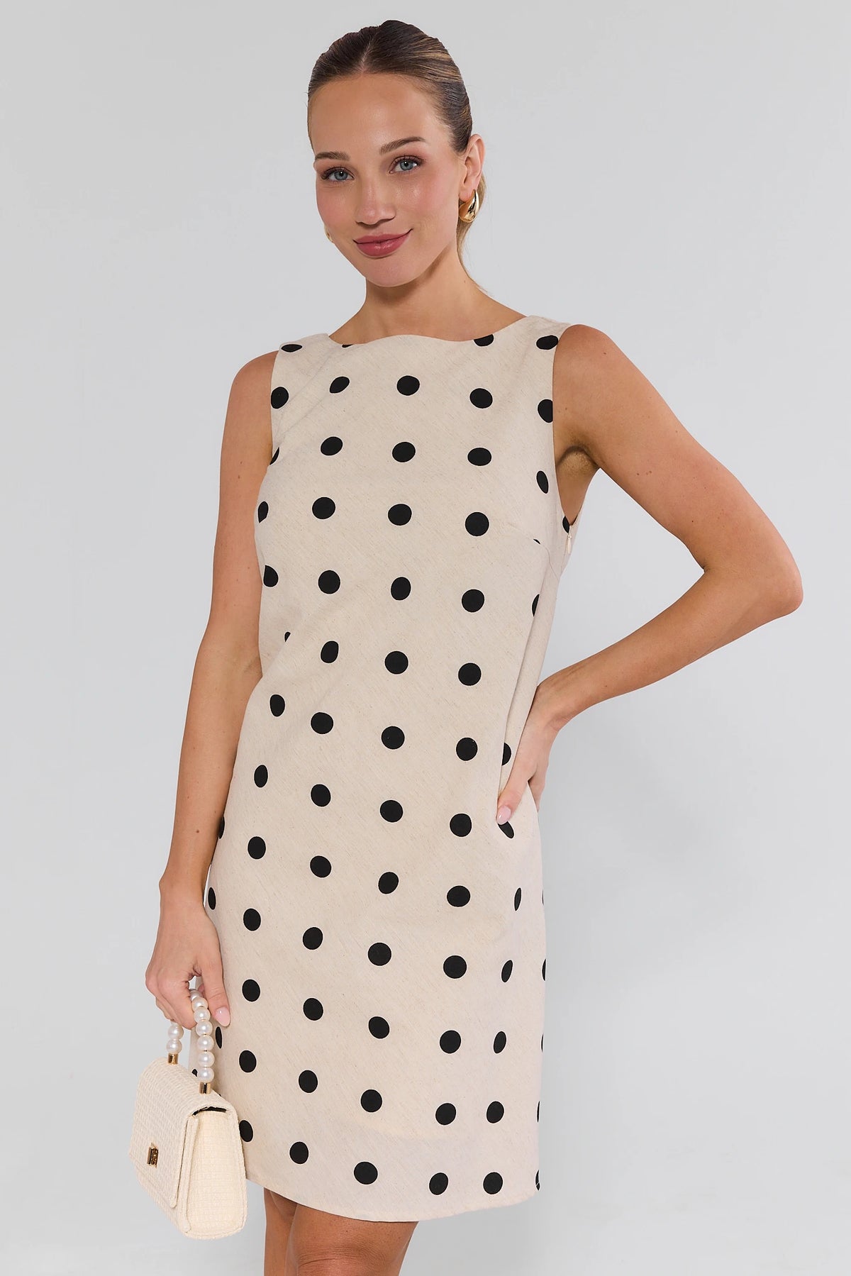 Woman wearing cream and black polka dot short dress with pearl bag - Front View | Avara