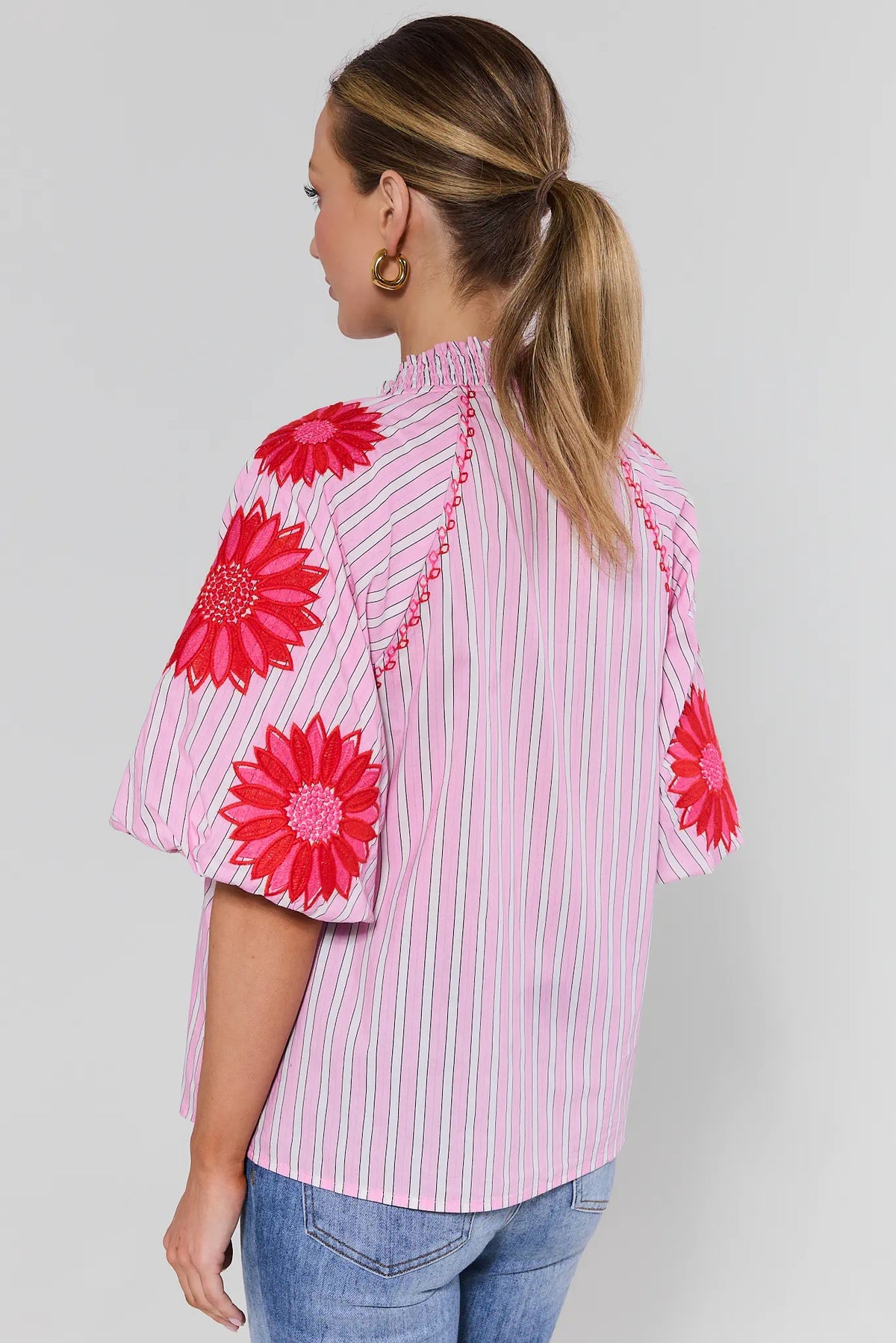 Back view of pink striped embroidered women's top with red floral appliqué sleeves and smocked collar | Avara