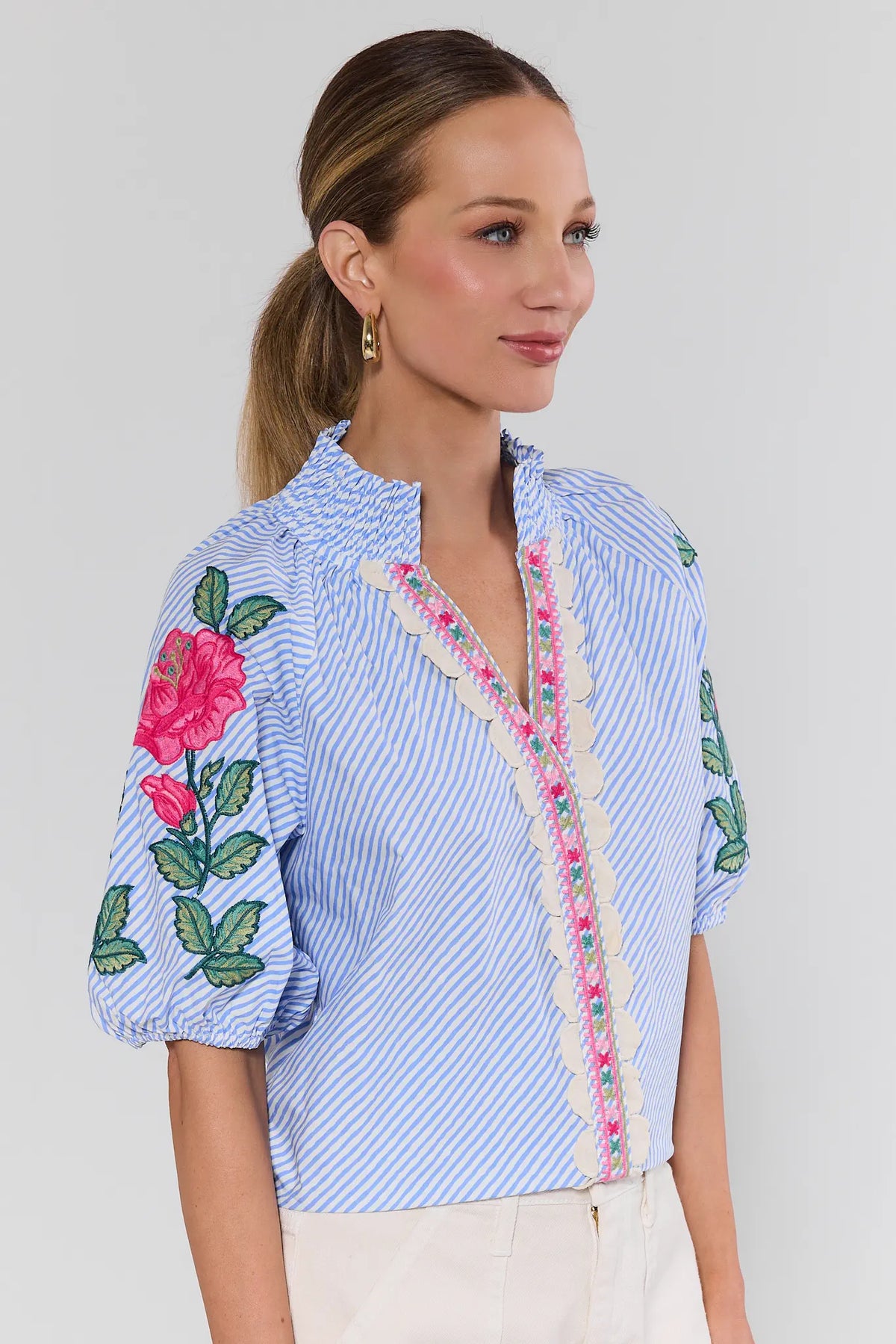 Woman wearing blue striped floral embroidered top with scallop trim and puff sleeves - Side Detail | Avara
