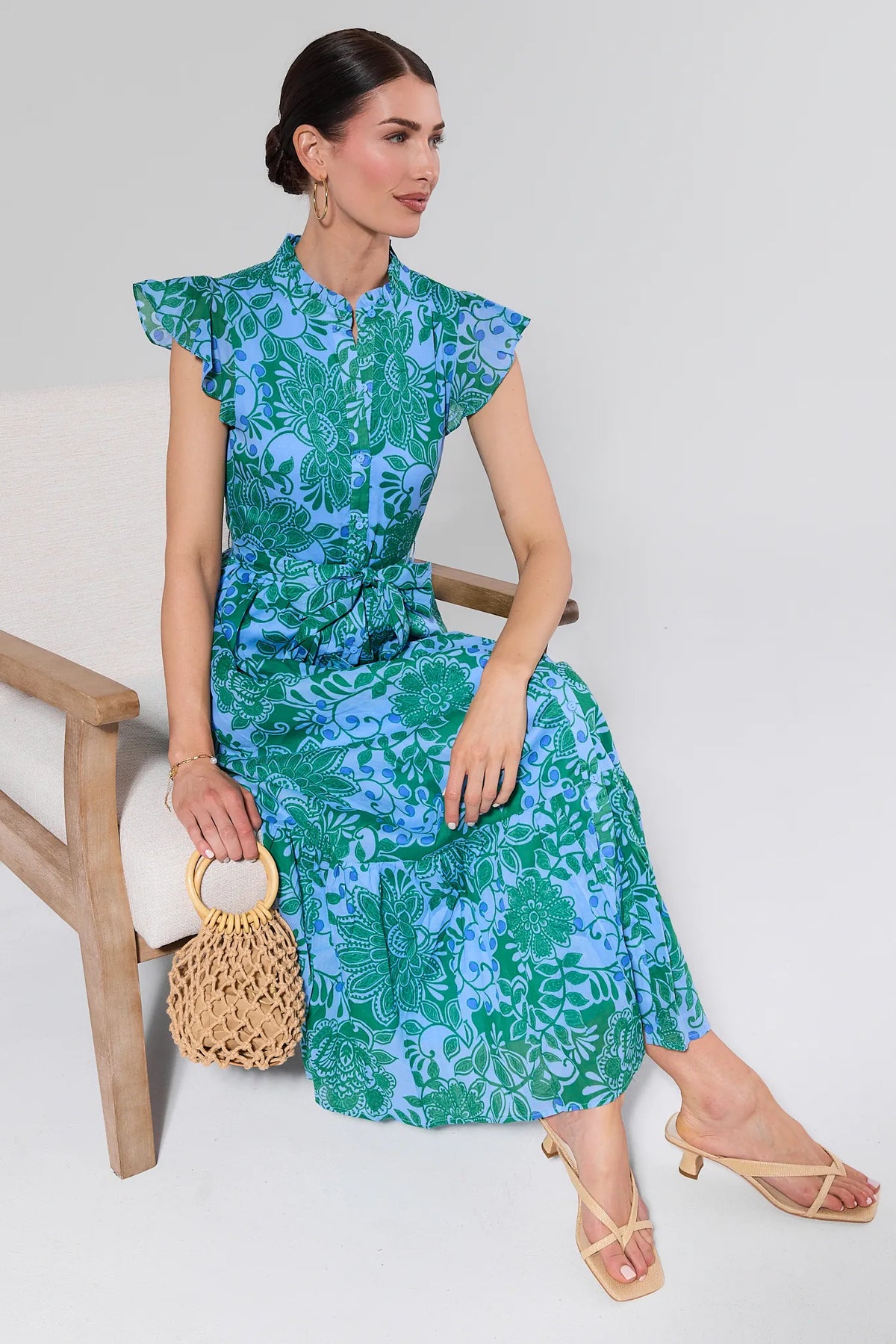 Woman wearing a blue and green floral dress holding a woven handbag.