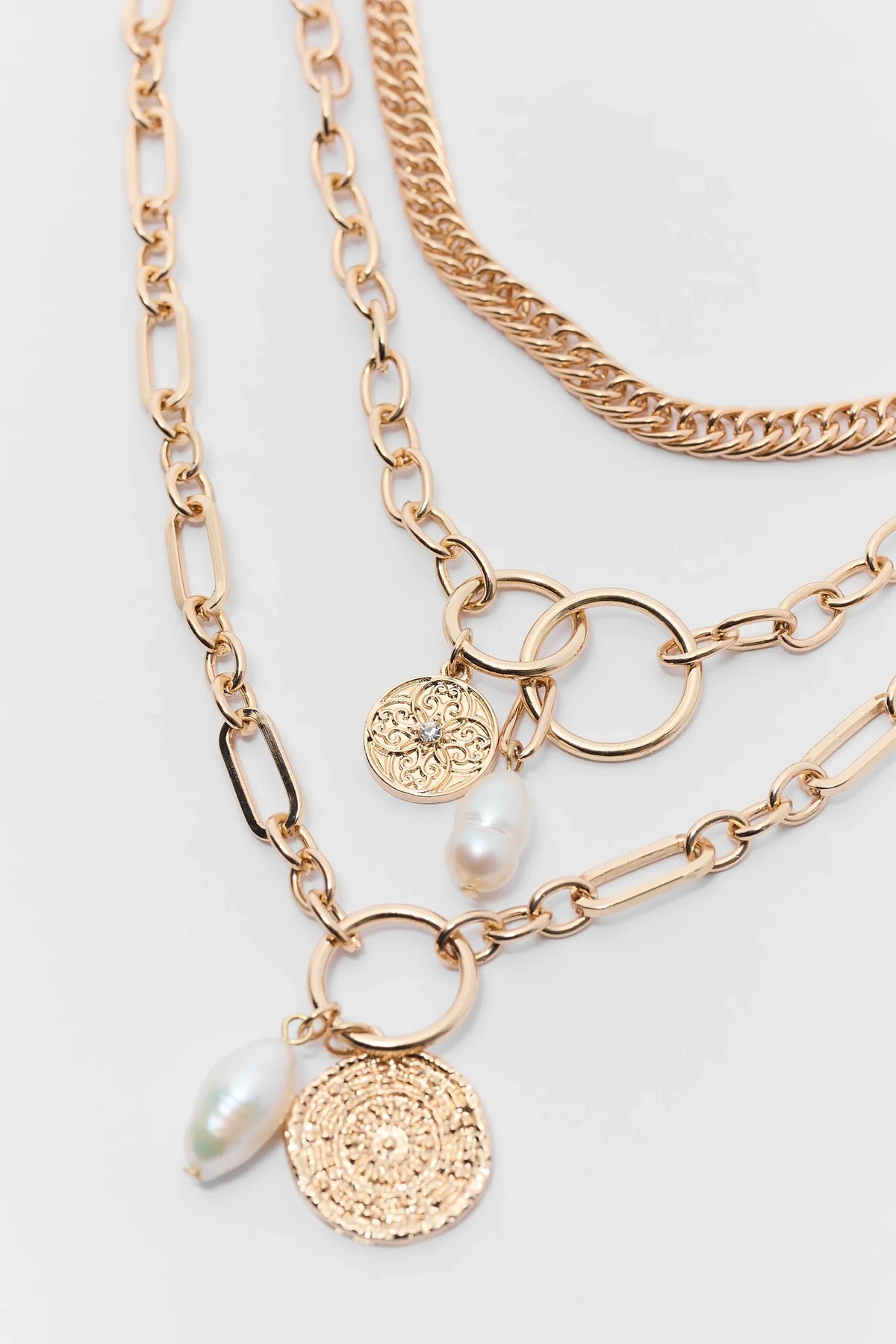 Gold layered necklace close-up detail showing coin charms, pearl drops, and mixed chain links | Avara