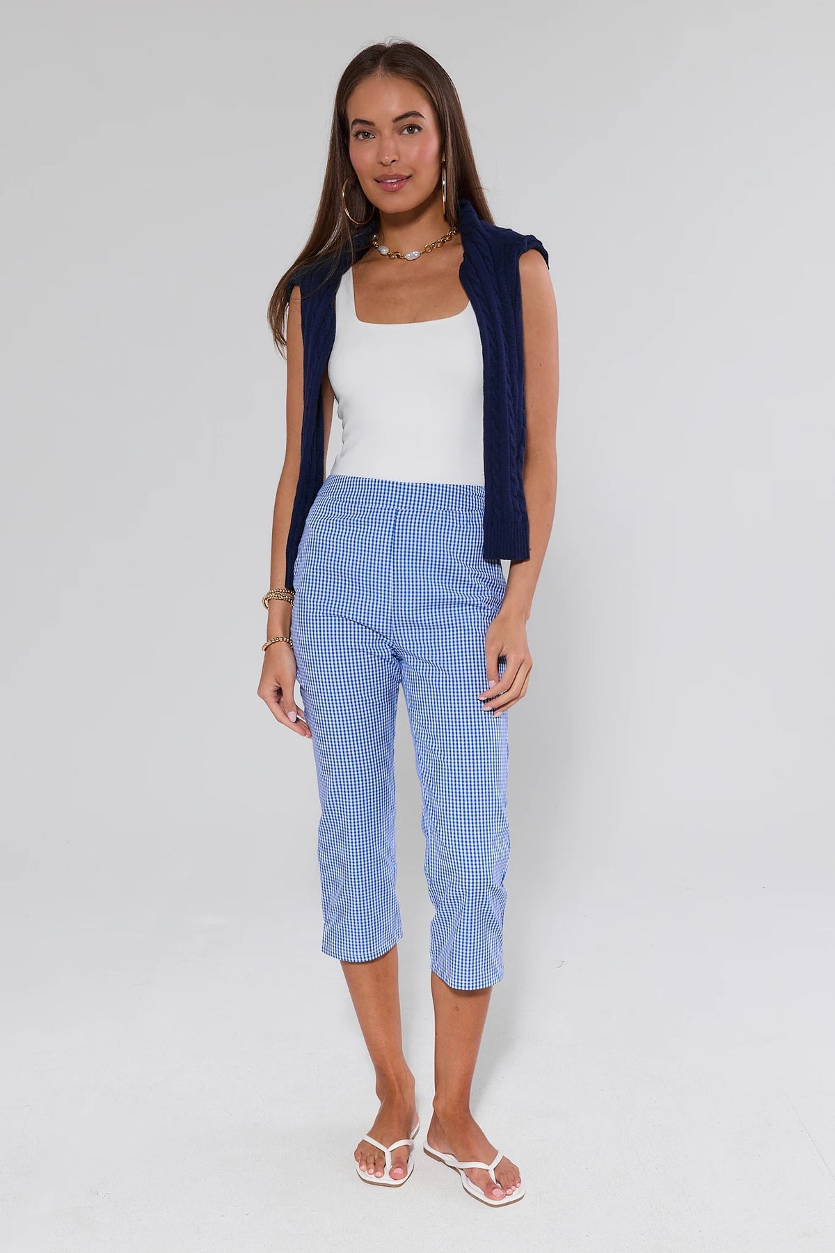 Woman wearing blue gingham capri pants styled with white tank and navy cable-knit vest, full outfit view | Avara