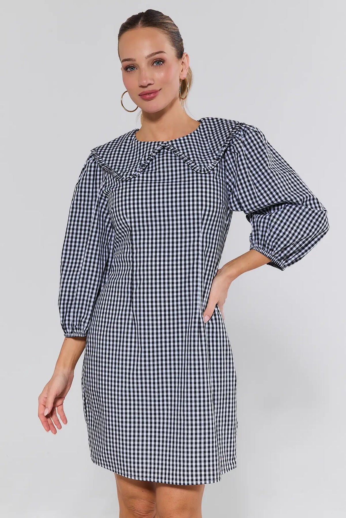 Woman wearing black gingham short dress with ruffle Peter Pan collar and puff sleeves - Front View | Avara