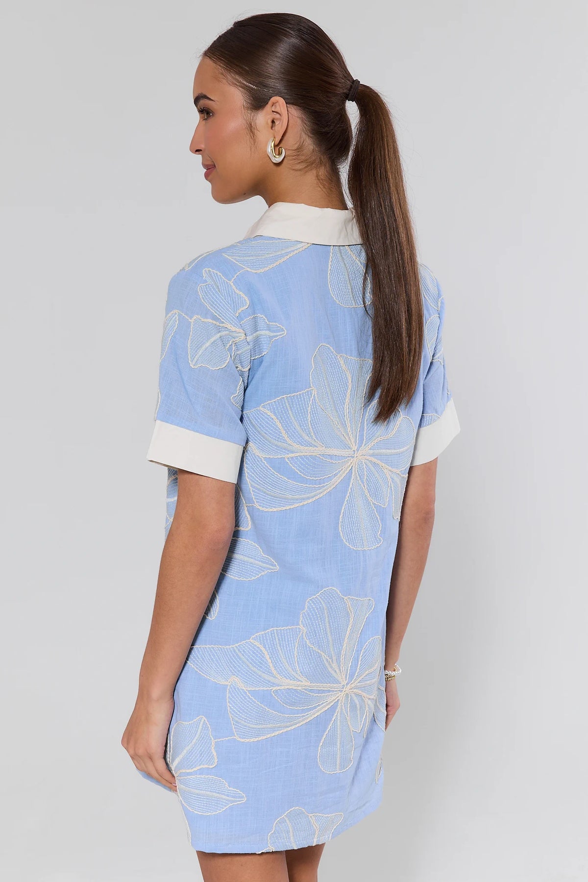 Woman wearing a light blue dress with white floral patterns on a plain background