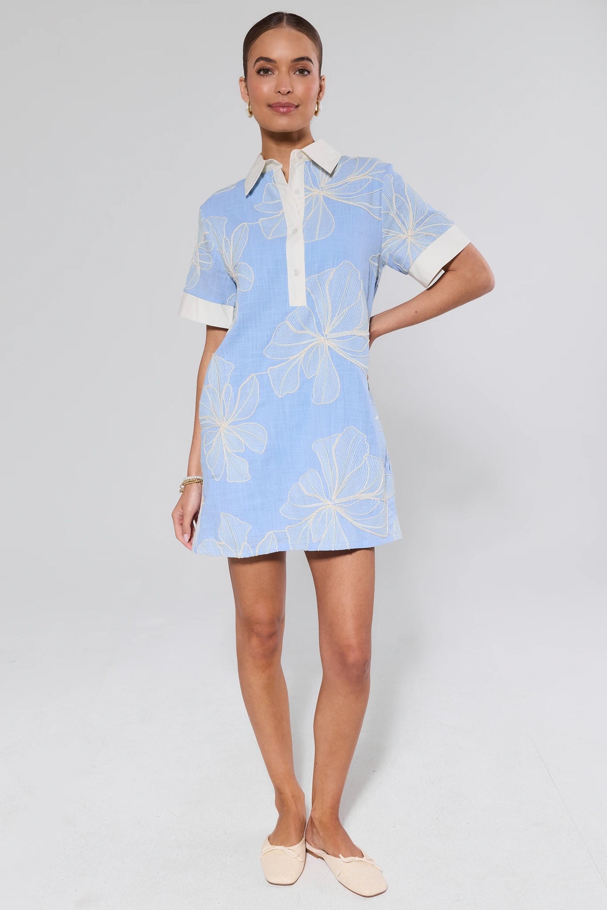 Woman wearing a light blue dress with white floral patterns on a plain background