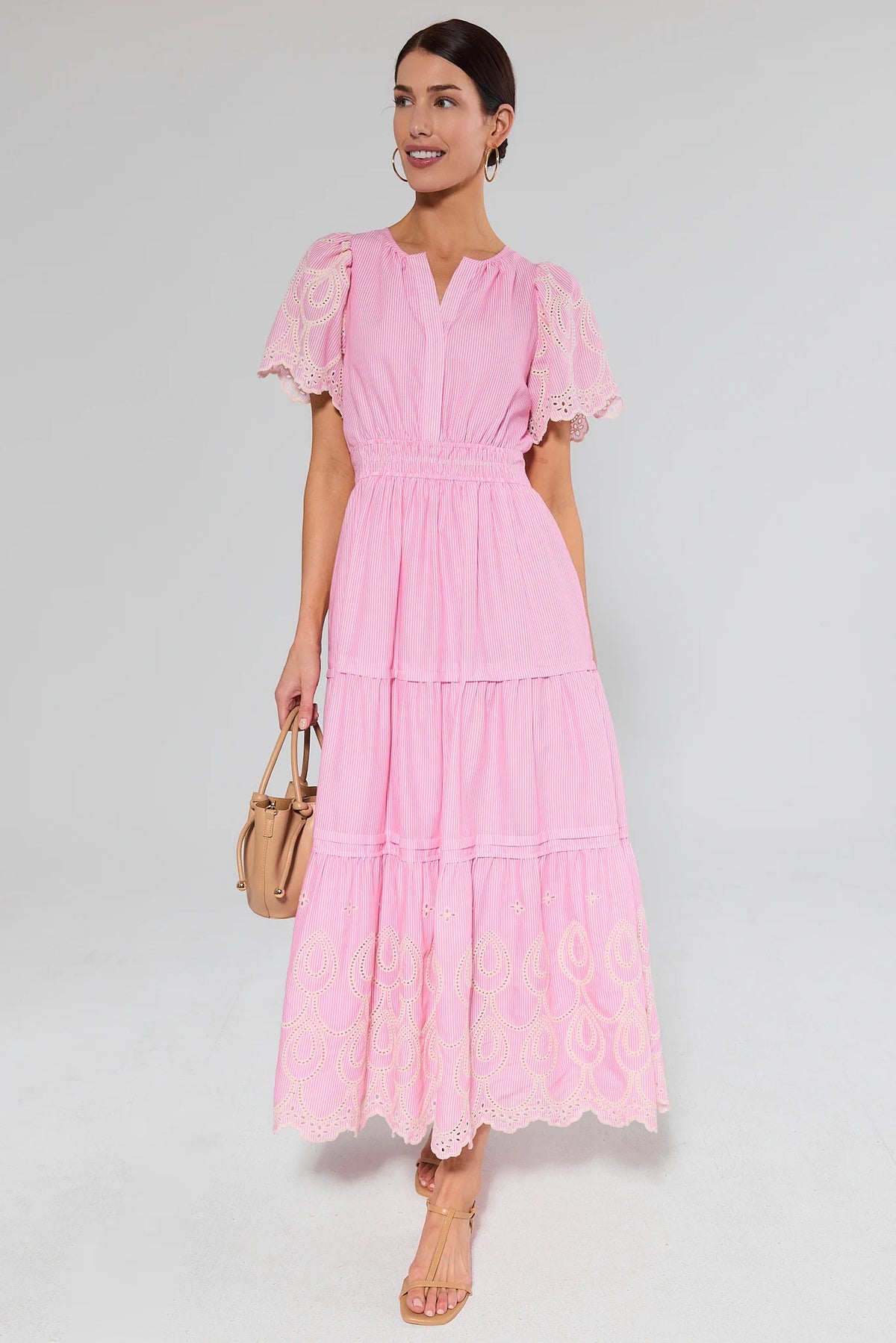 Woman wearing a pink dress with lace sleeves on a gray background with purse