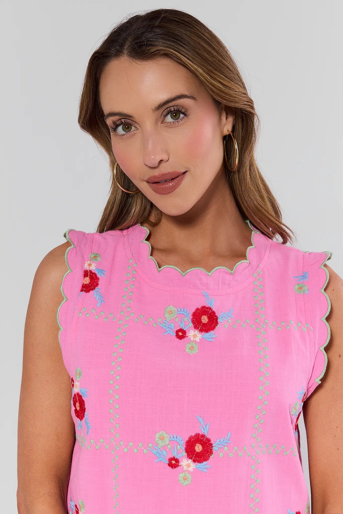 close up Woman wearing a pink dress with floral embroidery against a plain background
