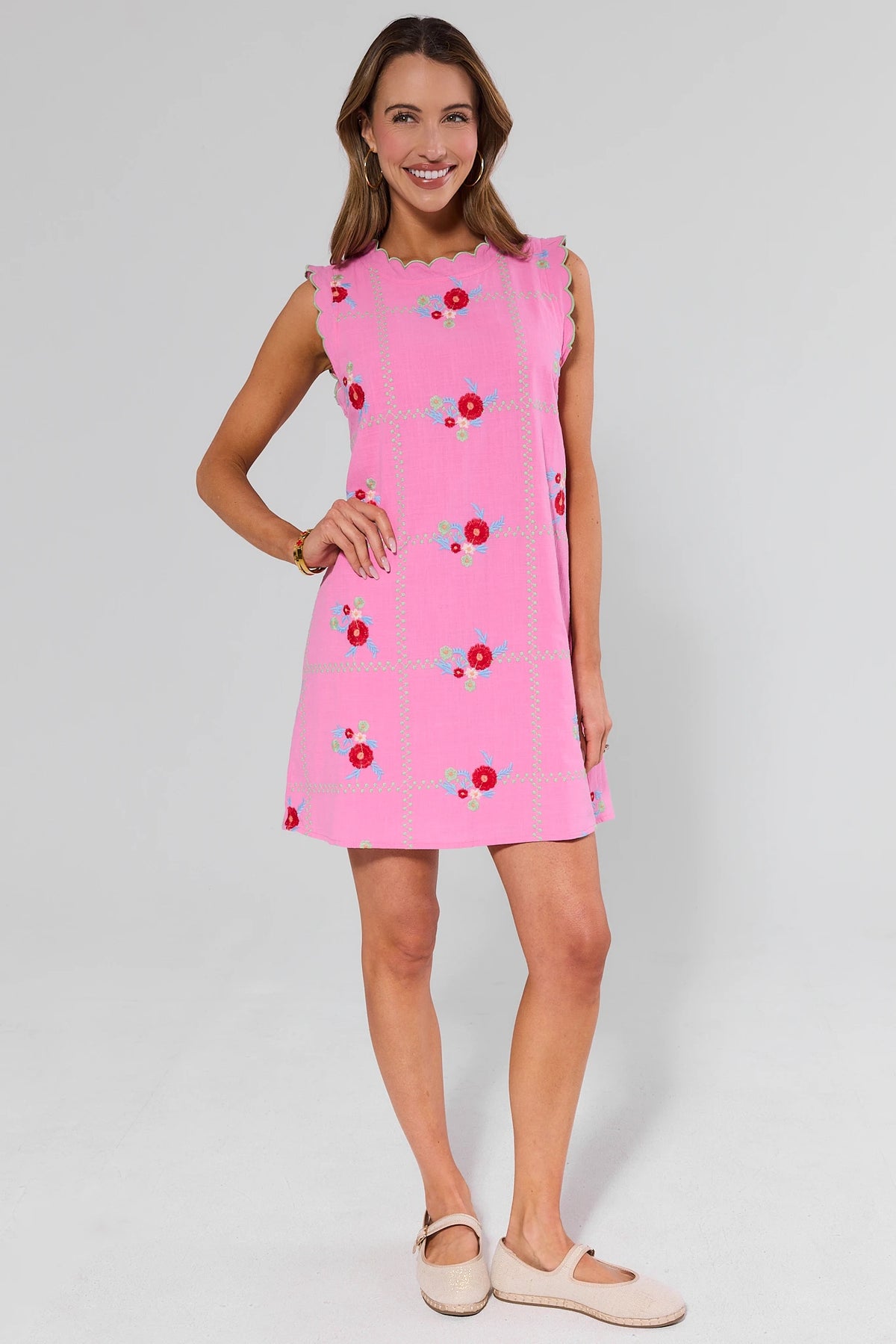 Woman wearing a pink dress with floral pattern and flats on a plain background