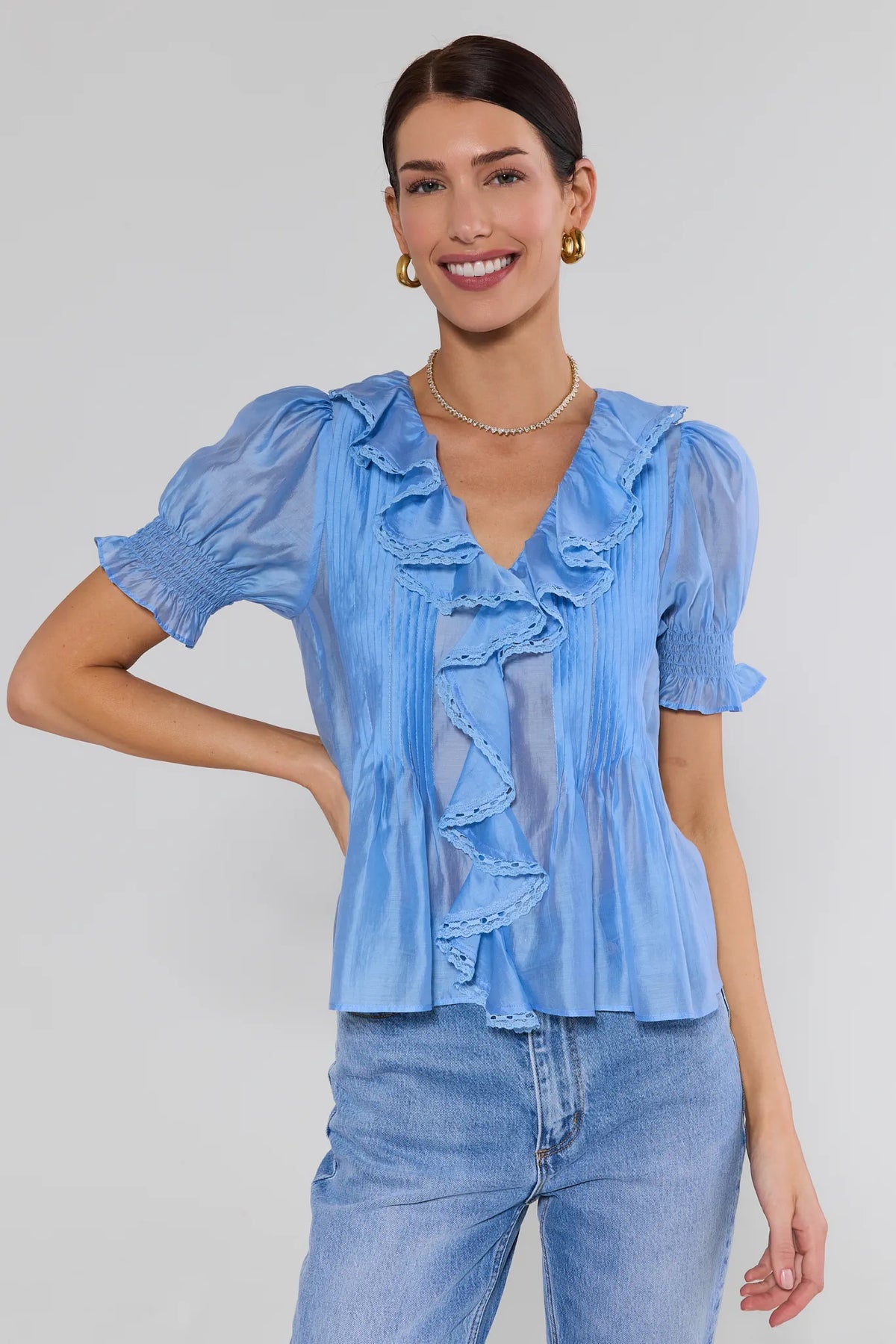 Woman wearing blue ruffle blouse with v-neckline and puff sleeves styled with blue jeans - Front View | Avara