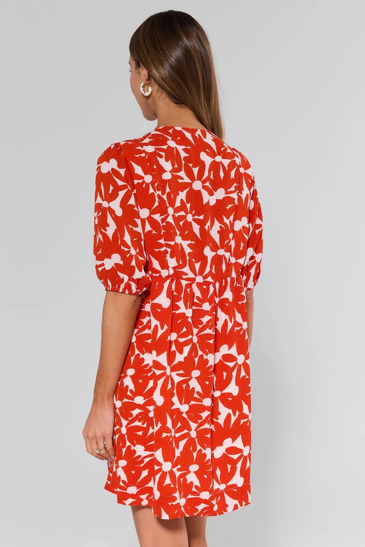 Woman standing wearing a red and white floral dress on a gray background