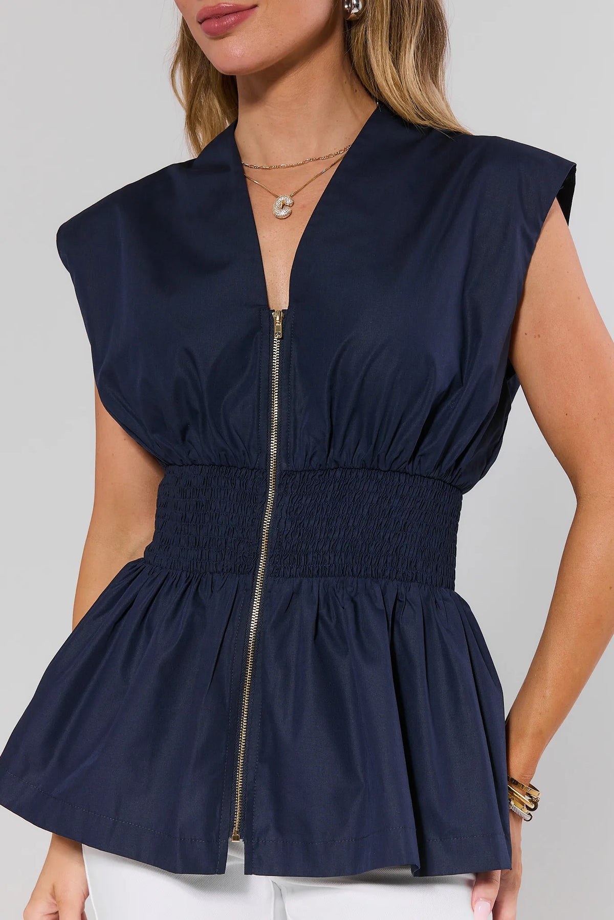 Close-up of navy peplum zip-up top showing gold zipper and smocked waist detail | Avara