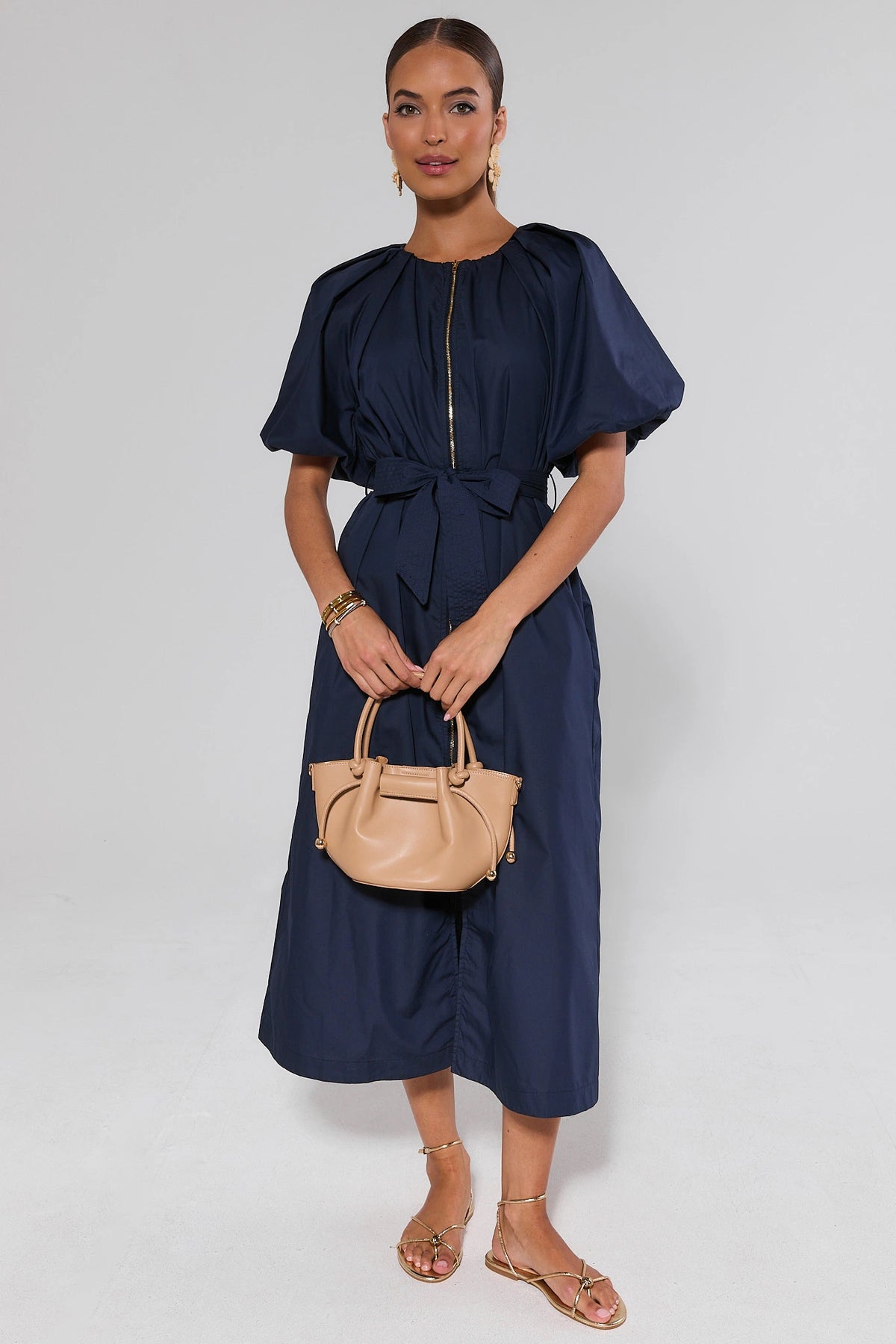 Woman wearing navy blue belted midi dress styled with gold sandals and beige handbag, full-length front view | Avara