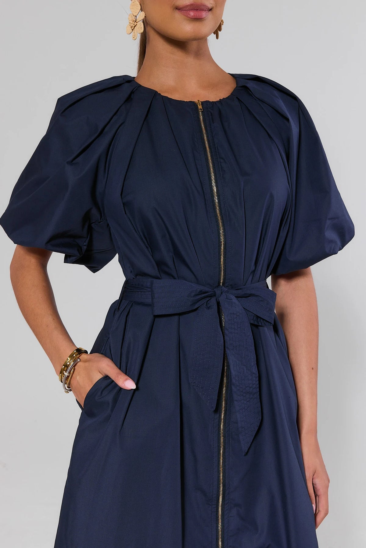 Close-up of navy belted midi dress showing gathered puff sleeves, tie waist belt, and gold zipper detail | Avara