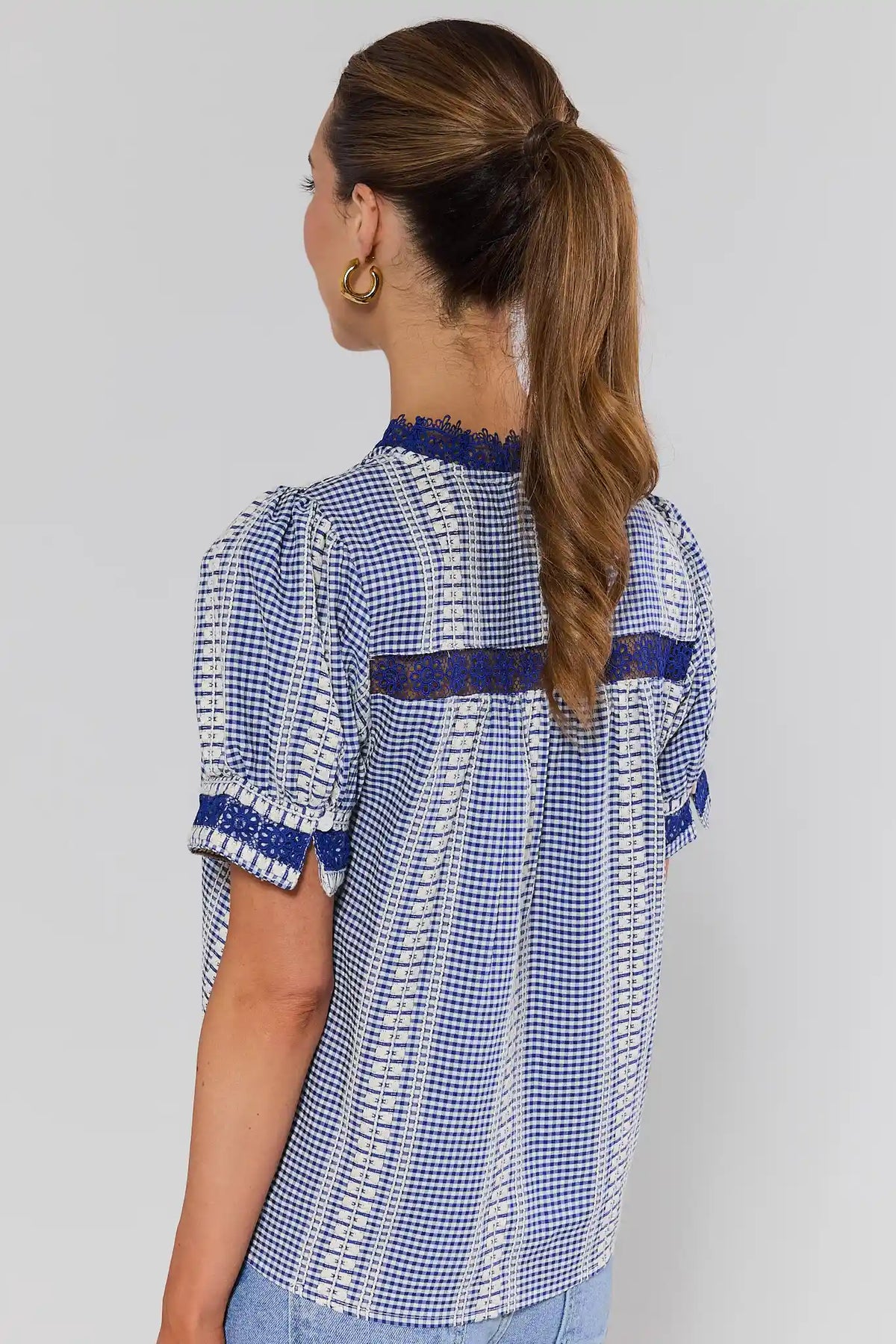 Woman standing wearing a blue and white checkered blouse with a plain background