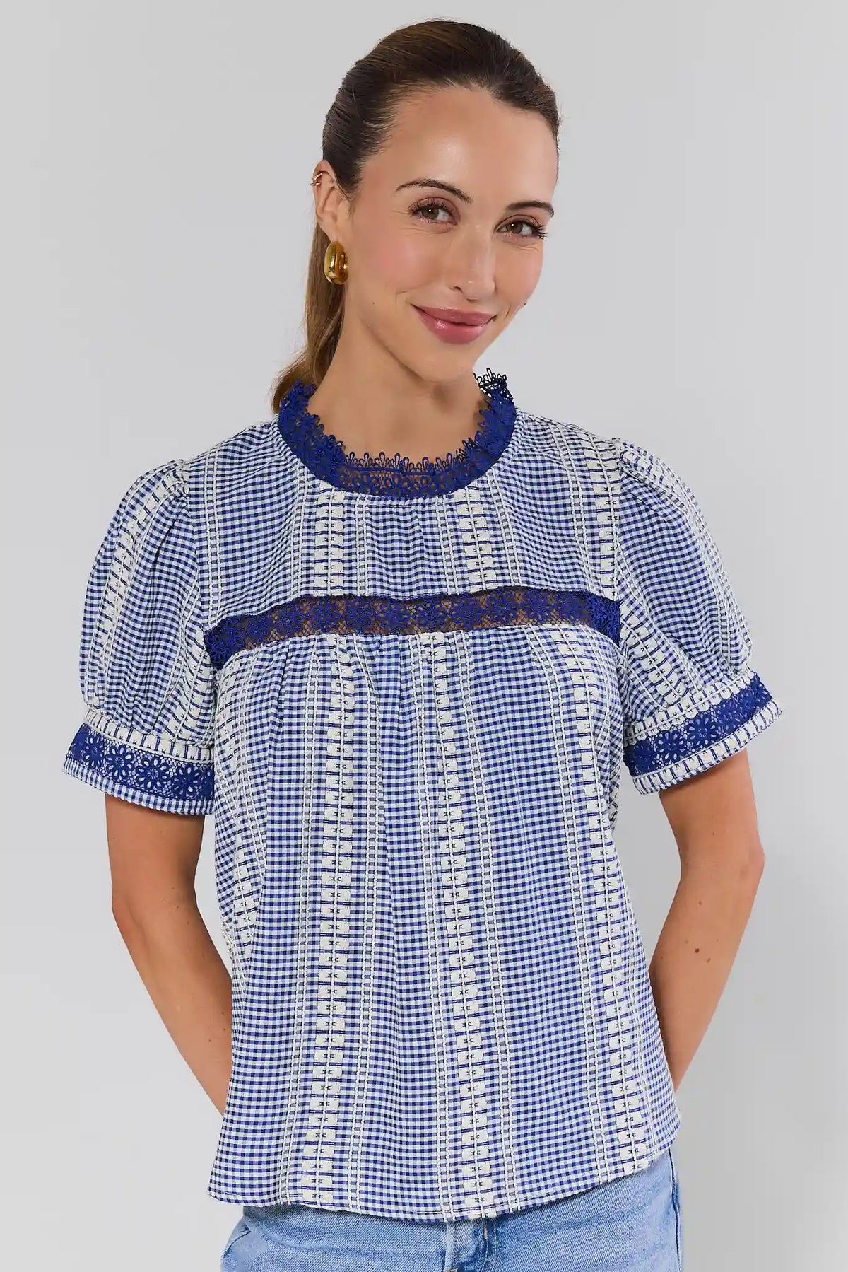 Woman wearing a blue and white checkered blouse with lace details on a gray background