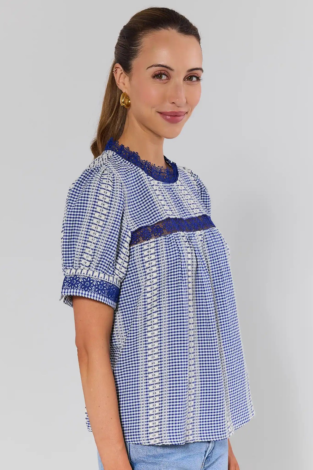 side shot Woman wearing a blue and white checkered blouse with lace details on a gray background