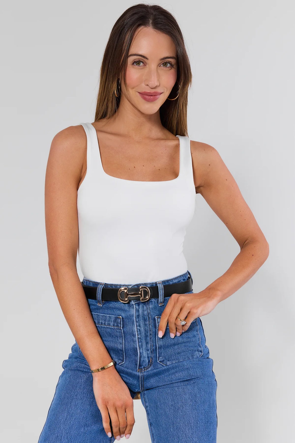 Woman wearing a white tank top and blue jeans against a plain background