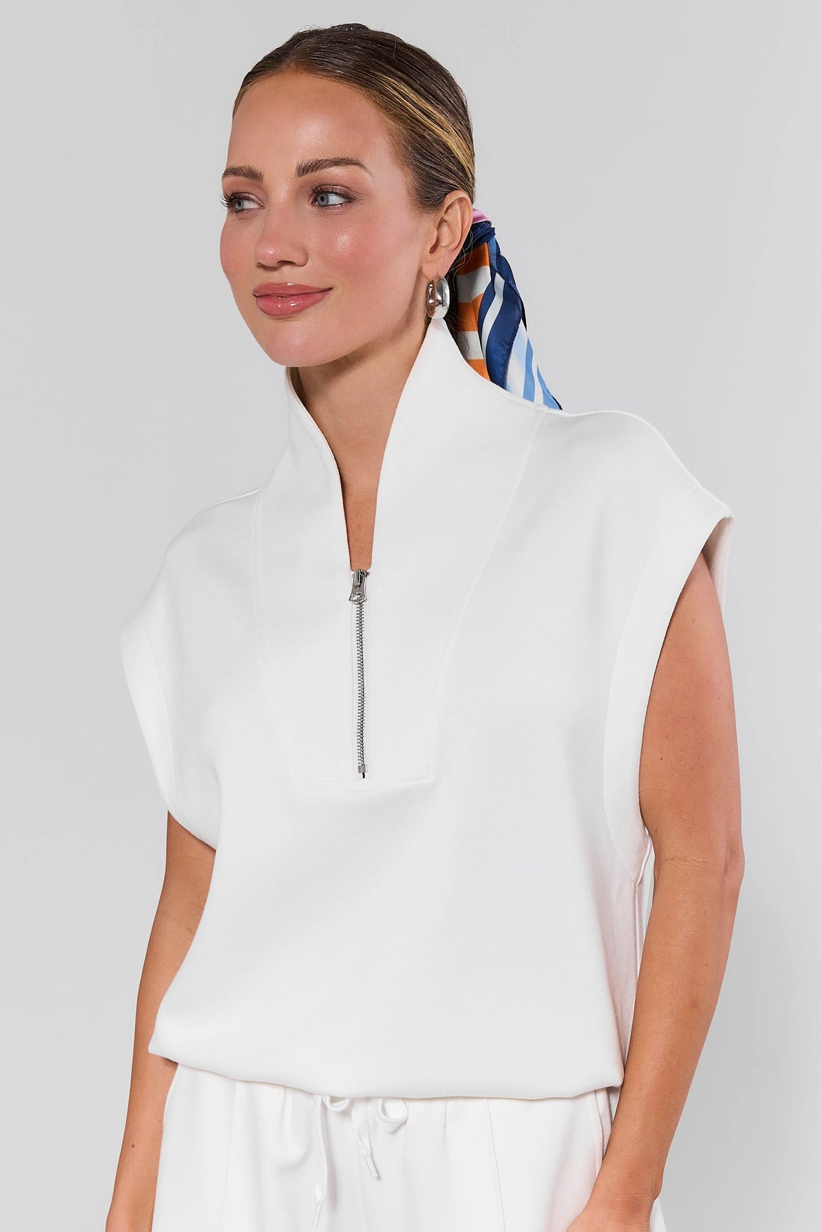 Woman wearing a white sleeveless top with a zipper on a plain background