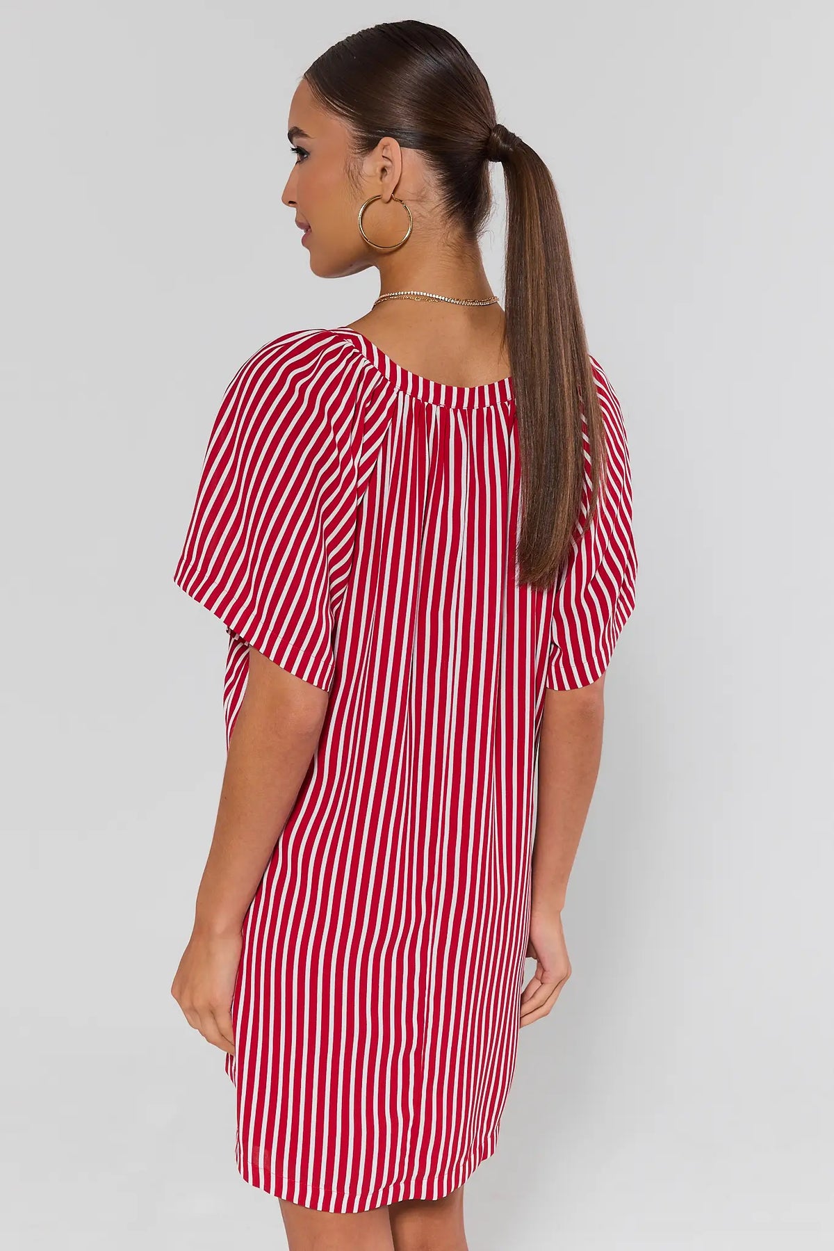 Woman standing wearing a red and white striped dress against a plain background