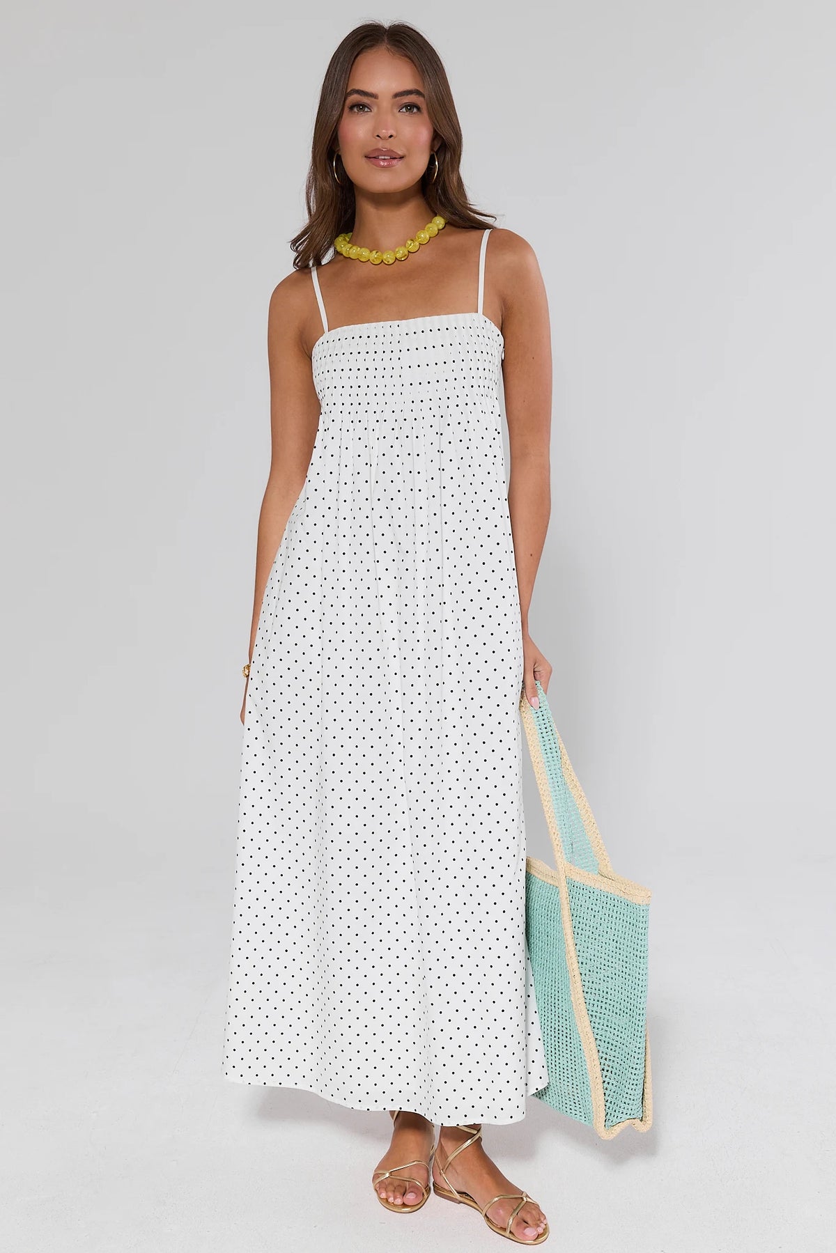 Woman wearing a white polka dot dress holding a green bag on a gray background