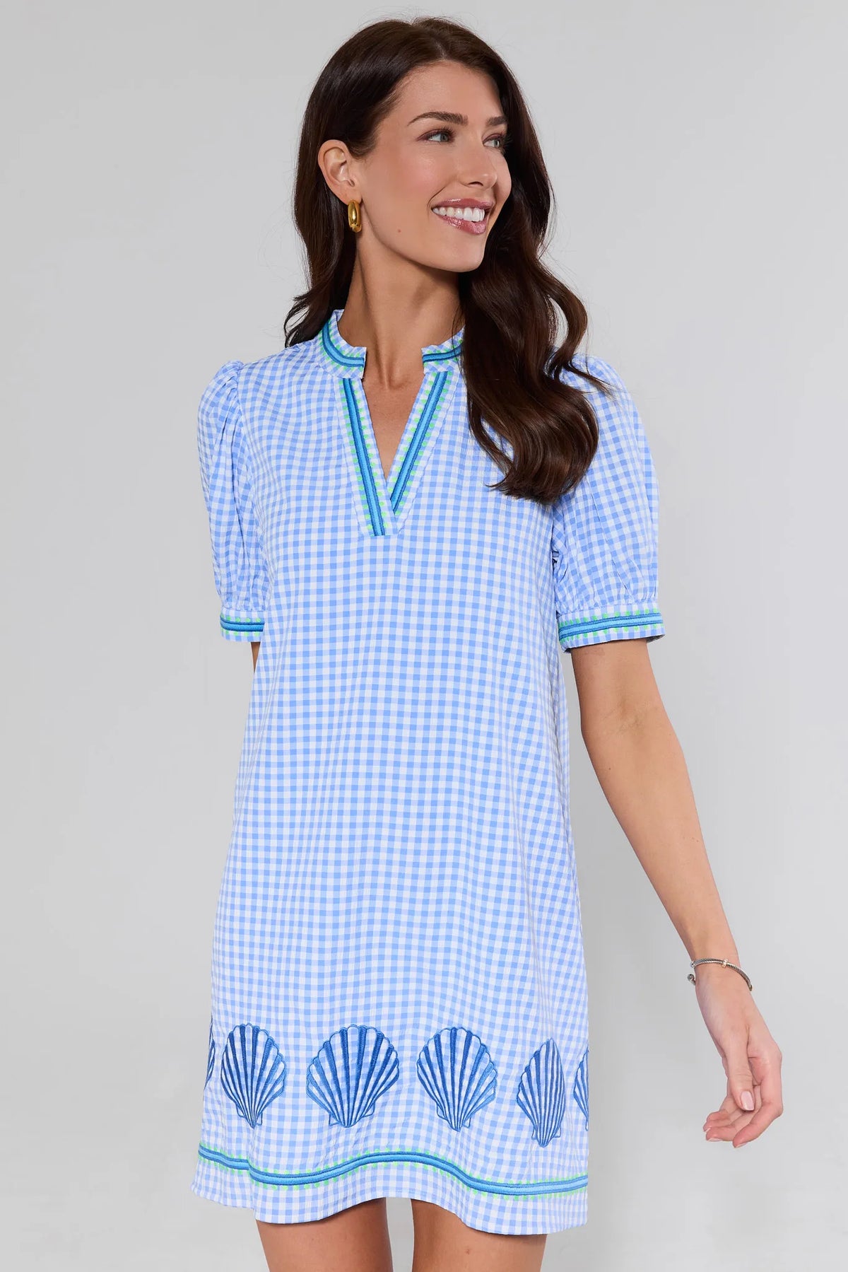 Woman wearing a blue checkered dress with shell patterns on a plain background