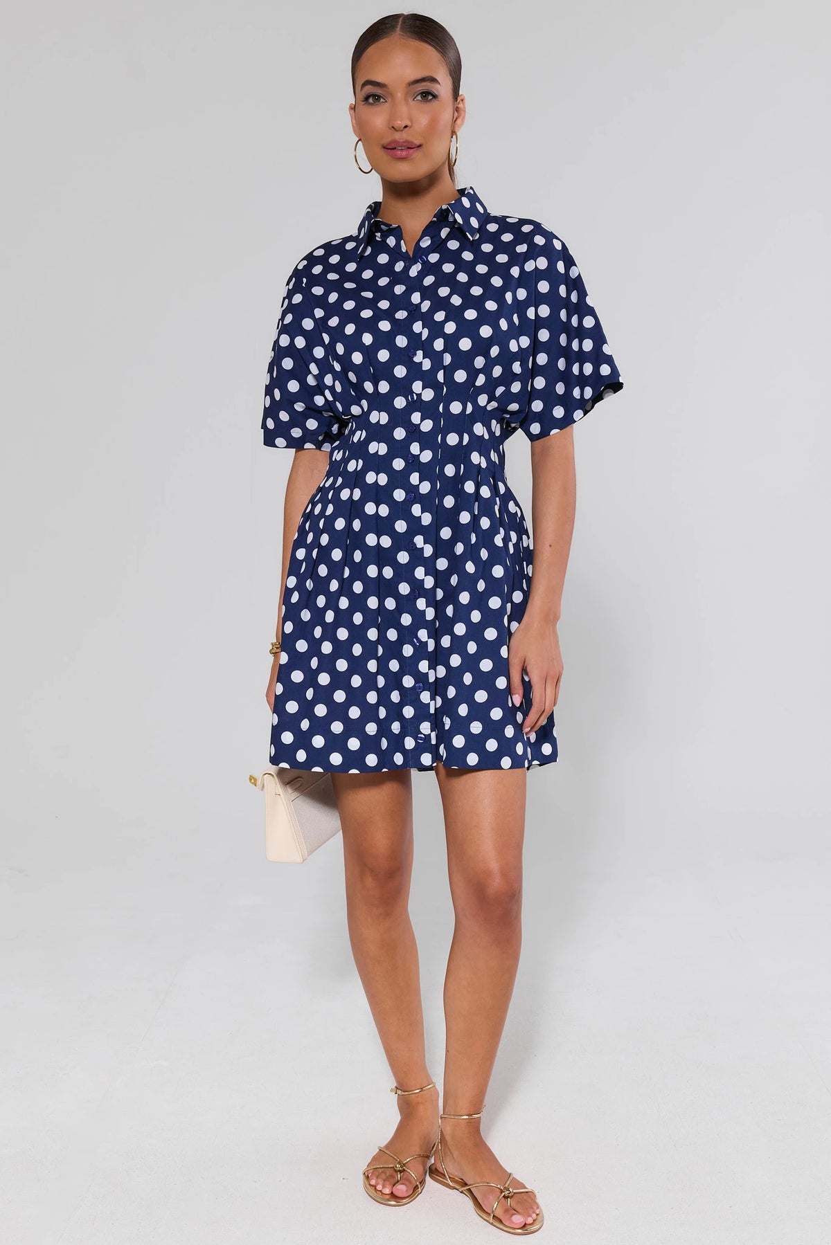Addison Navy Polka Dot Short Dress styled with gold sandals and cream clutch - Full Length Front | Avara