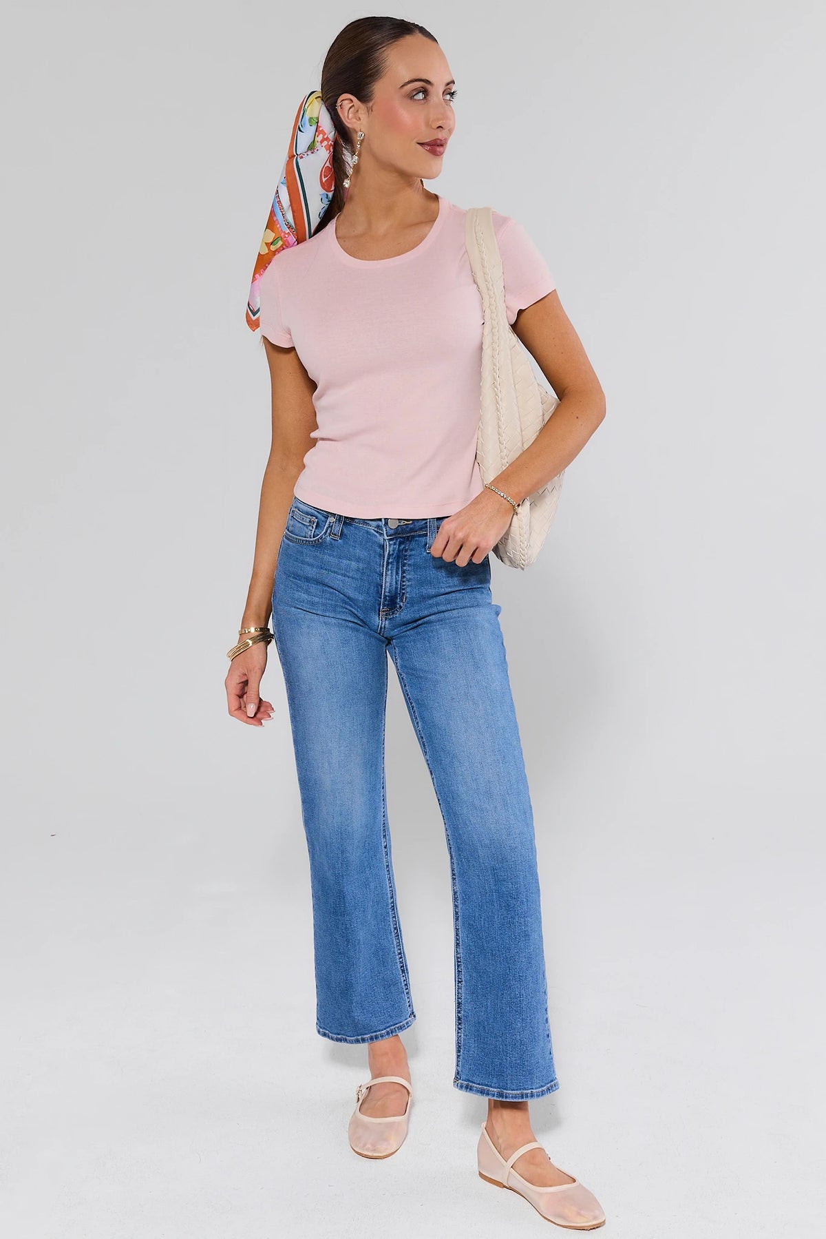 Woman wearing a pink top and blue jeans with a white background