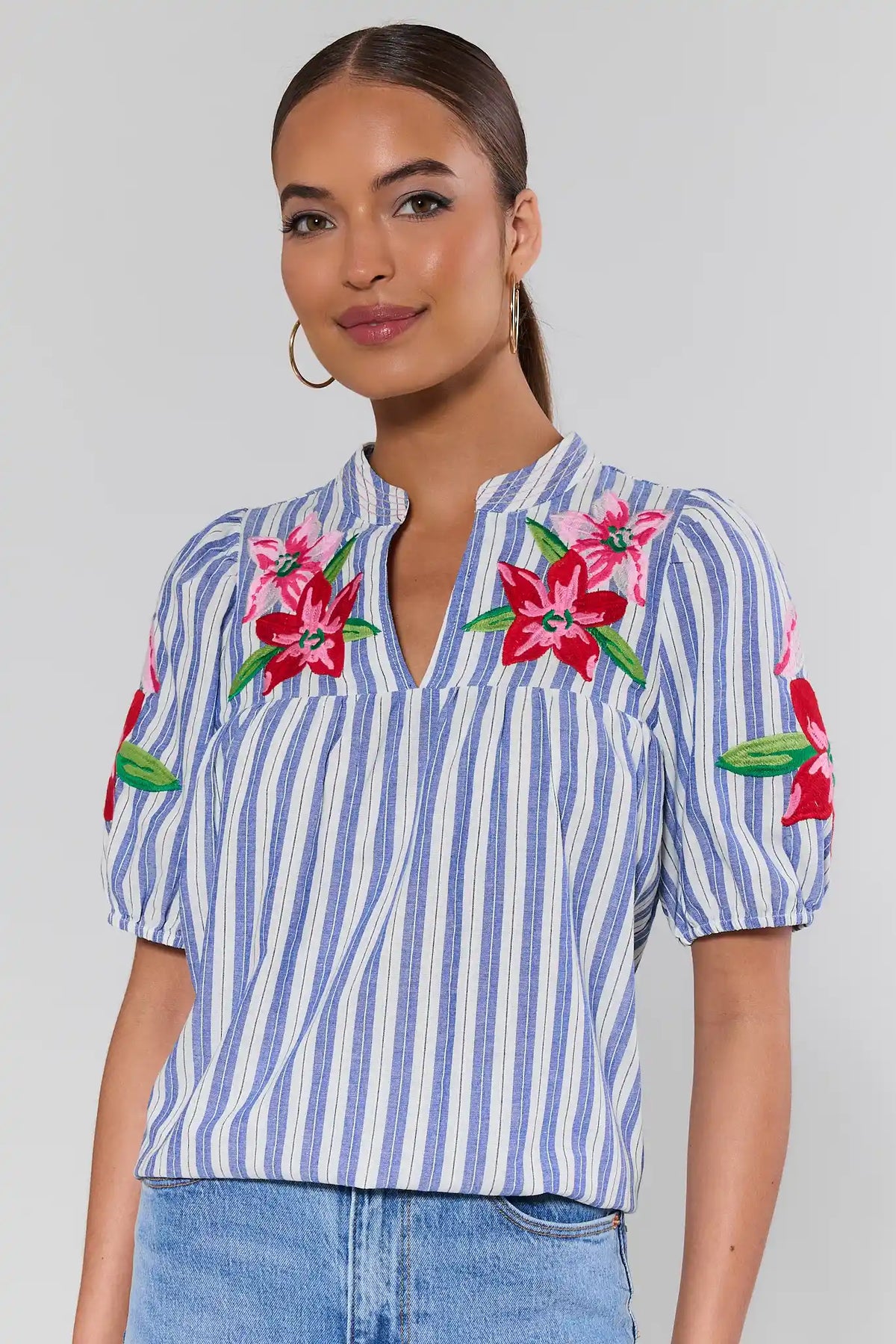 Woman wearing a blue and white striped lakesyn shirt with floral embroidery on a plain background