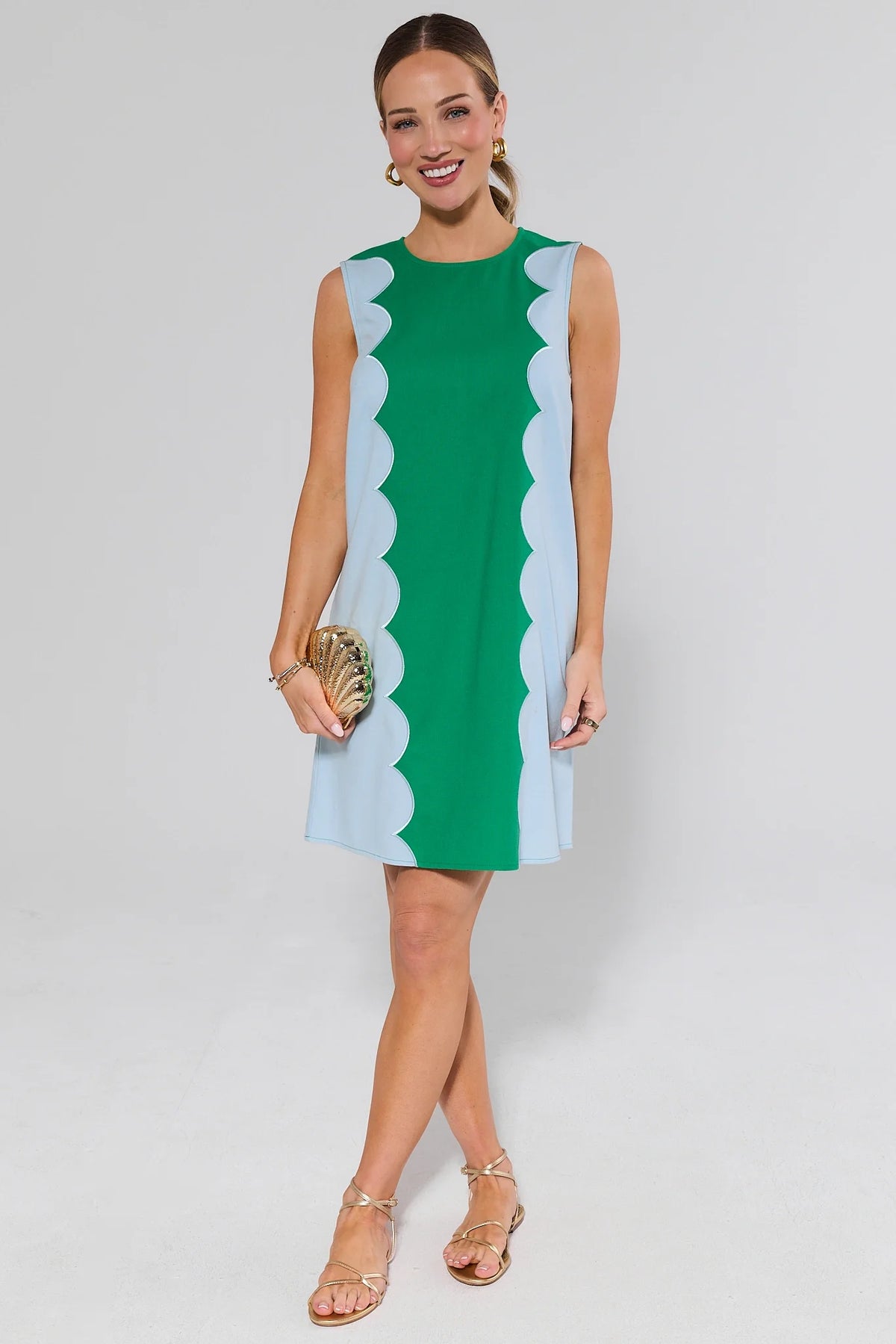 Woman wearing a caroline green dress with white scalloped edges on a plain background