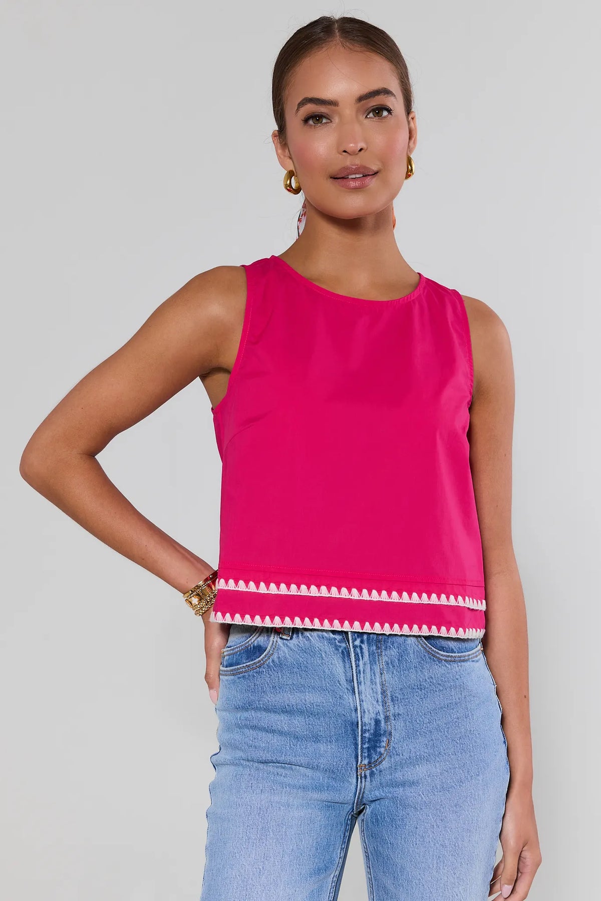Woman wearing a bright pink sleeveless top with white trim against a gray background