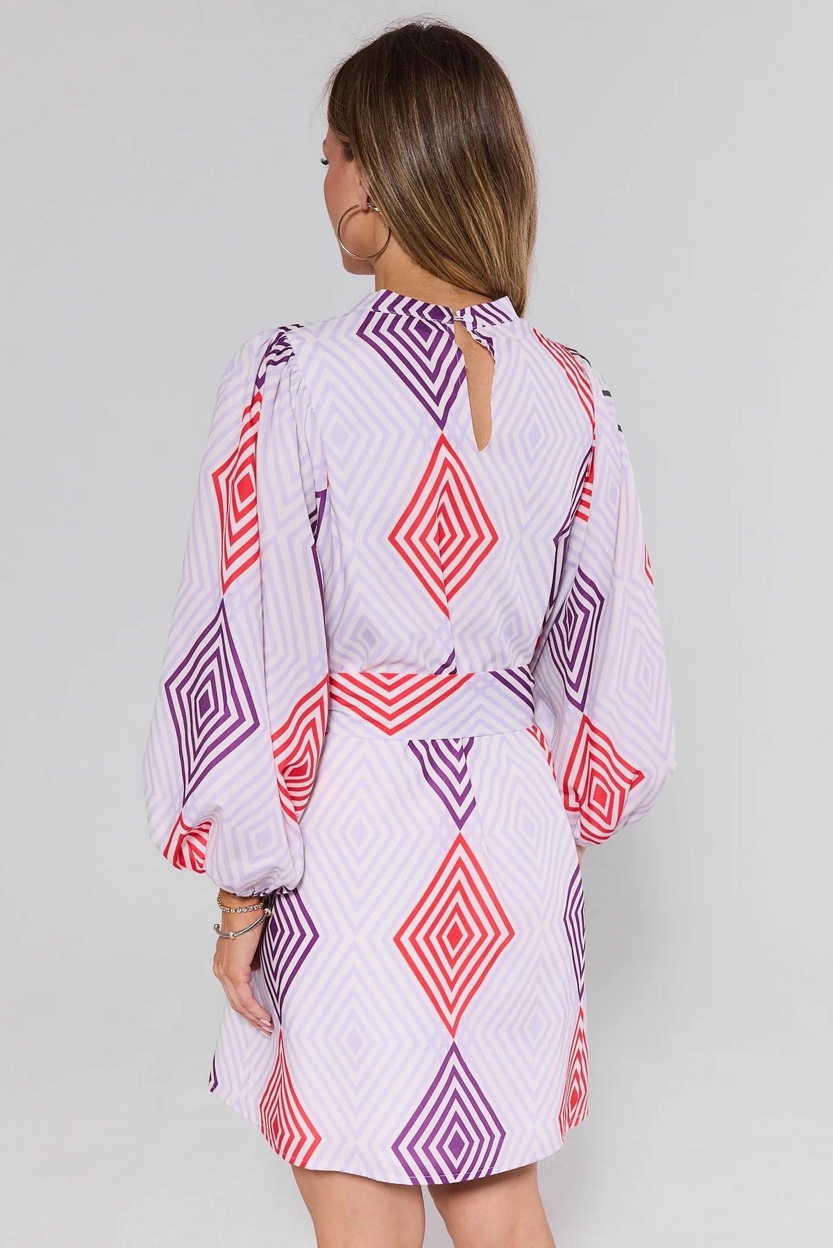 Woman standing wearing a patterned dress with geometric designs on a plain background