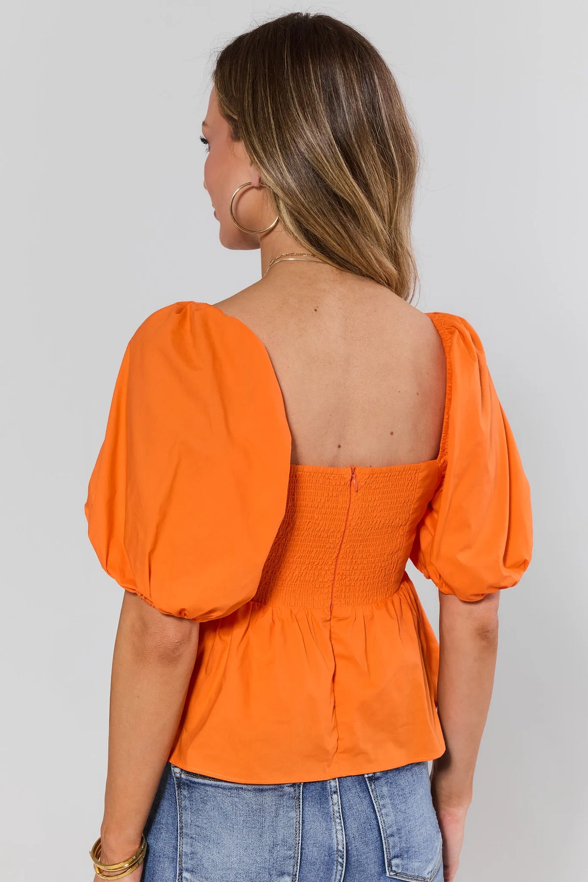 Back view of orange peplum top showing smocked bodice, hidden zip, and voluminous puff sleeves | Avara