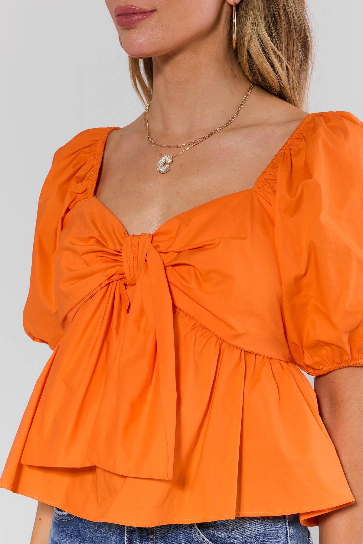 Close-up of orange peplum blouse sweetheart neckline and center tie knot detail with puff sleeves - Detail View | Avara