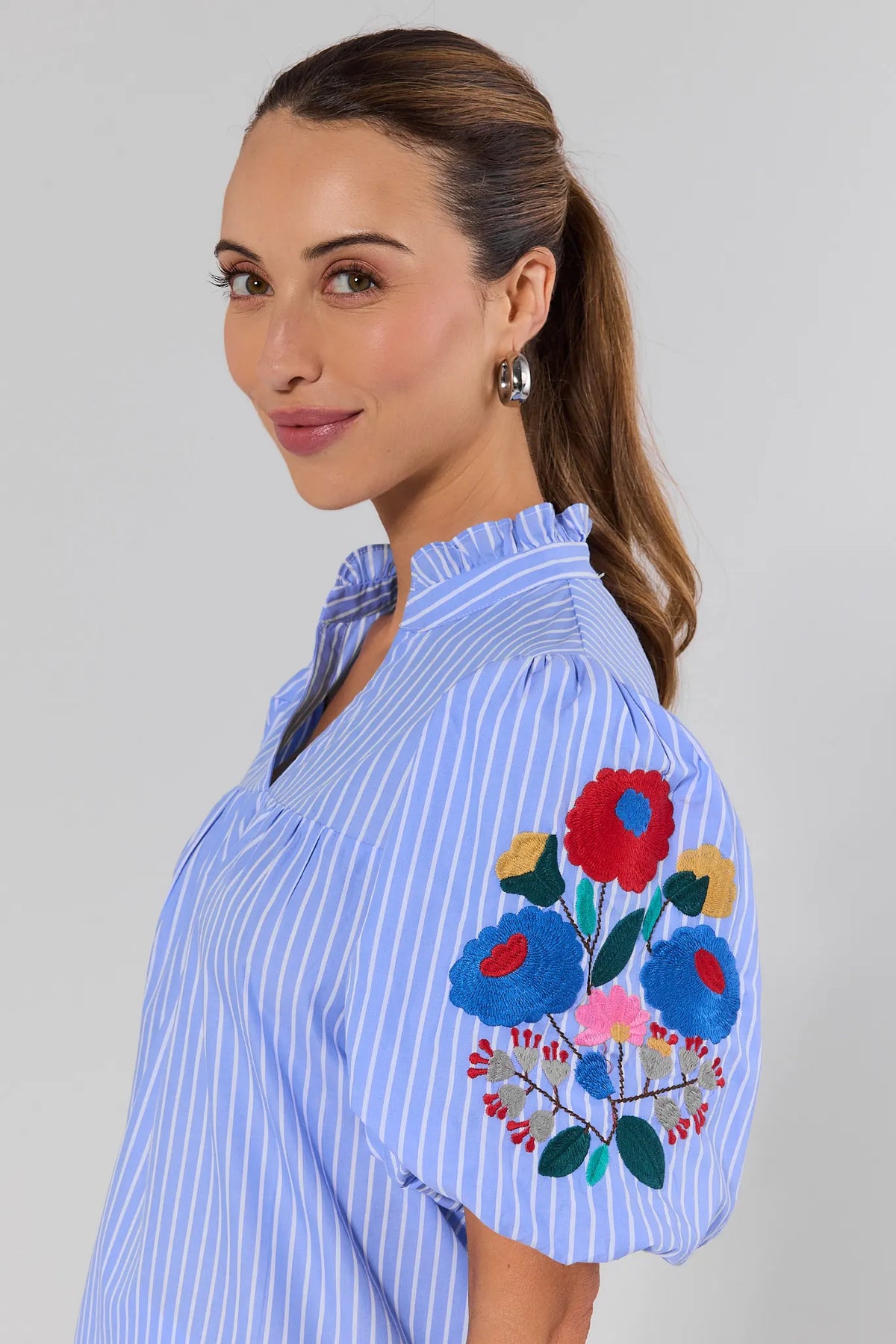 close up Woman wearing a blue striped shirt with floral embroidery on a plain background