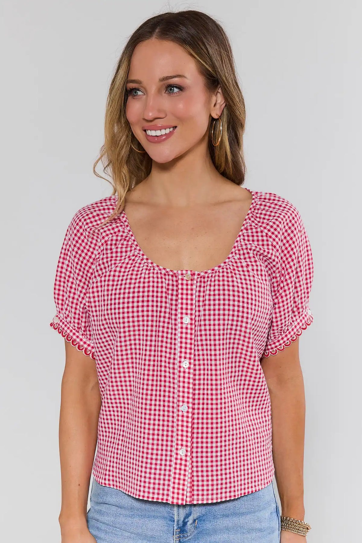 Women's red gingham button-up top with scalloped sleeves and scoop neckline, styled with light-wash jeans — Front View | Avara