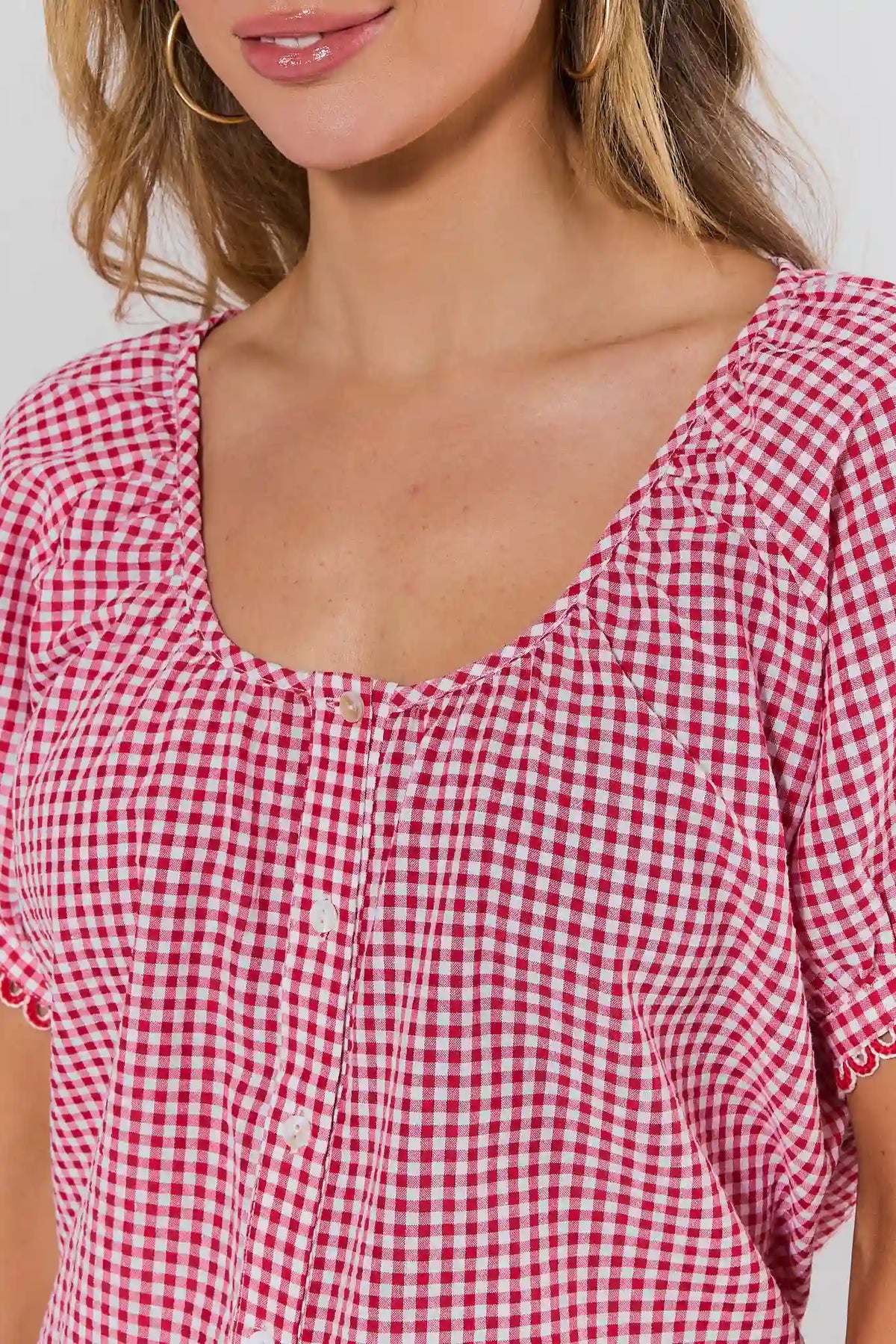 Red gingham button-up top close-up showing scoop neckline, button placket, and scalloped sleeve trim — Detail View | Avara