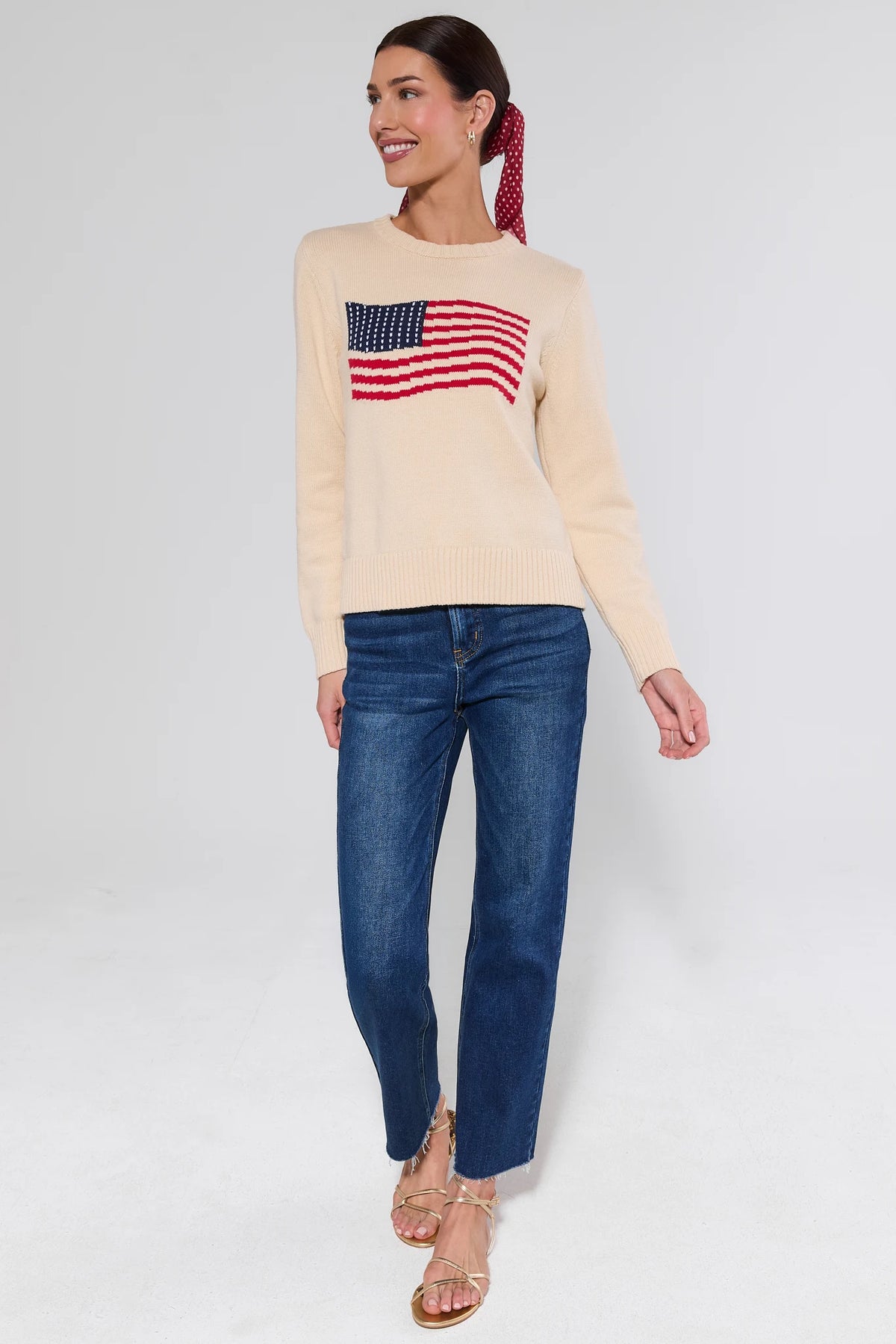 Cream American flag knit sweater on model, full-length side view with red scarf and gold sandals | Avara
