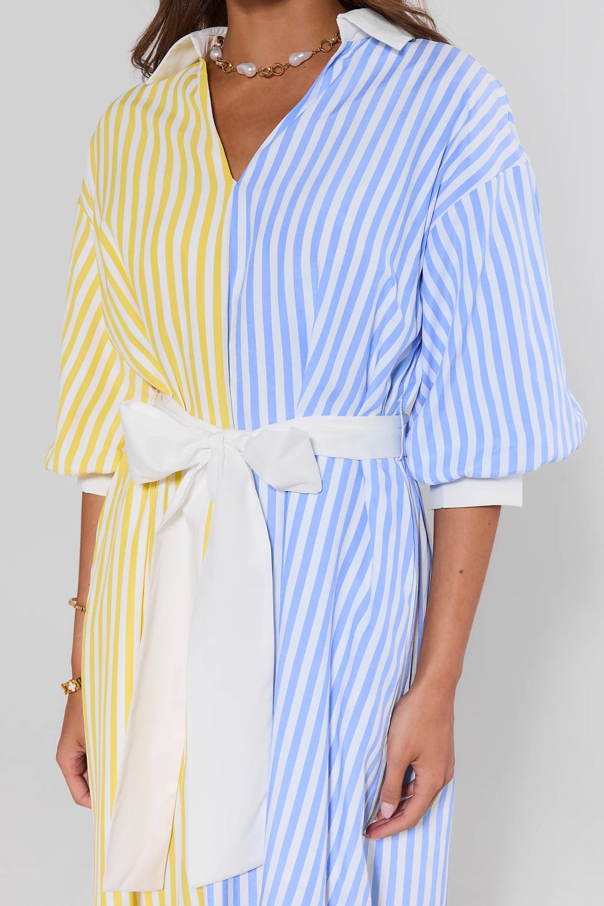 Close-up of blue and yellow striped midi dress white bow tie-belt and V-neckline detail | Avara