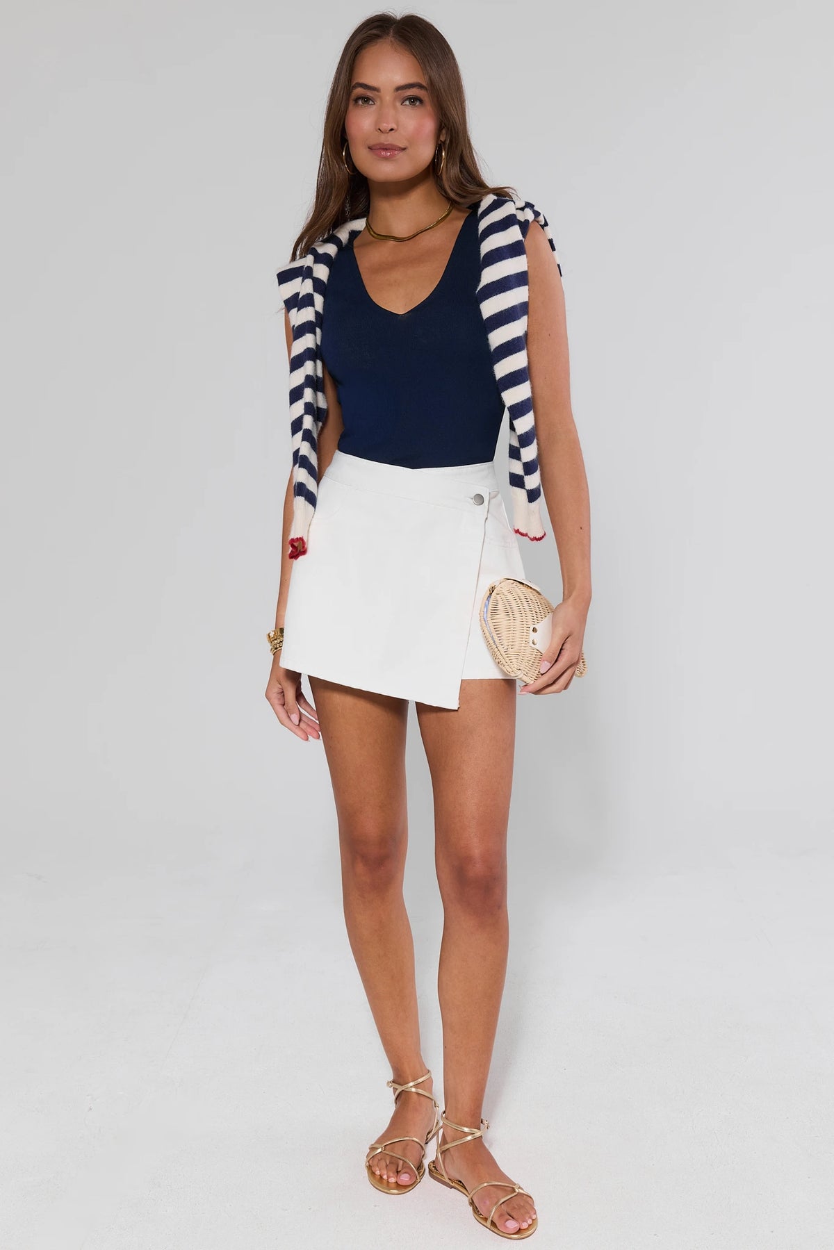 Woman wearing white denim wrap skort with navy top and striped cardigan, styled with gold sandals - Full Look | Avara