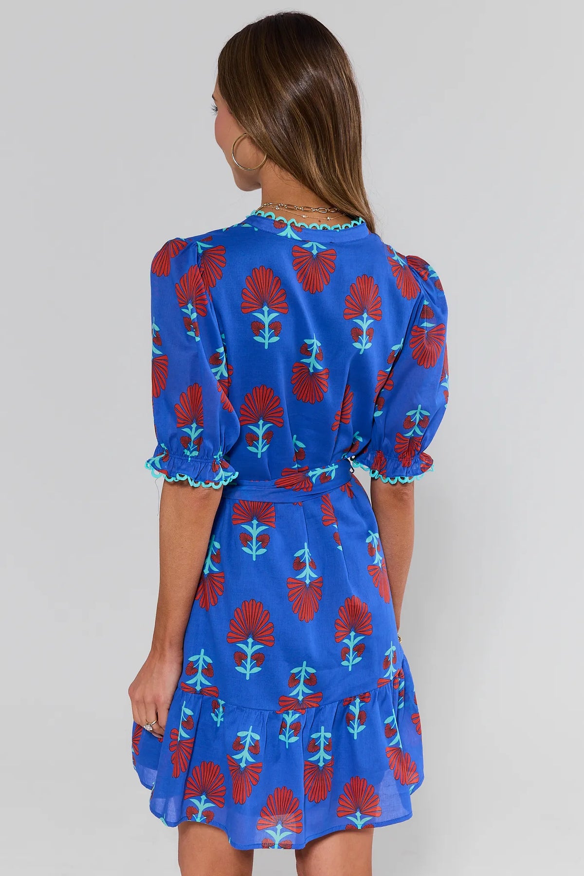 Woman standing wearing a blue dress with red and green floral pattern on a plain background