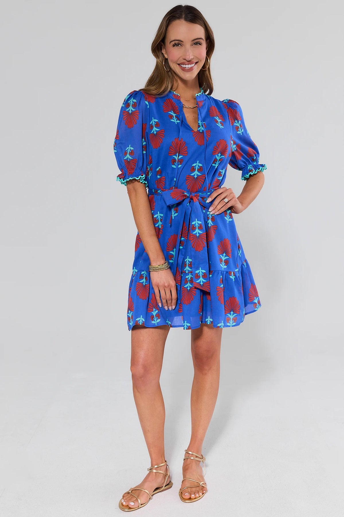 Woman wearing a blue dress with red floral pattern and sandals on a white background