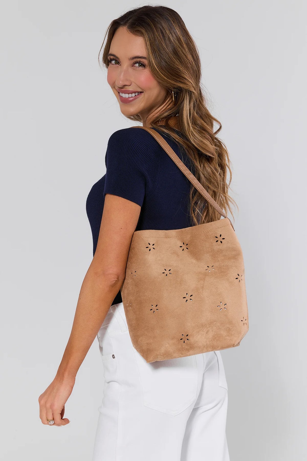 Woman carrying a tan leather bag with cut-out designs on a plain background