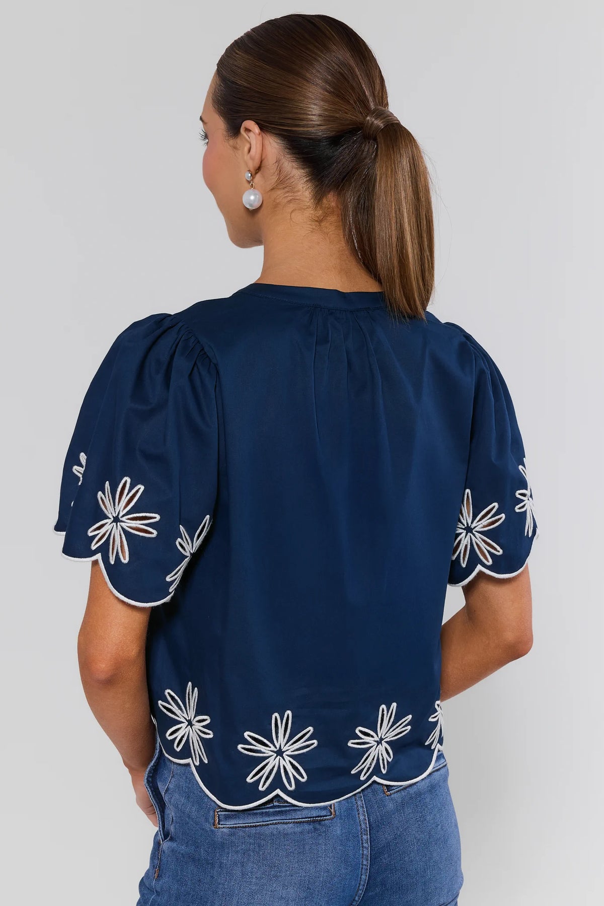 Navy blue embroidered top back view showing puff sleeves, white daisy eyelet scalloped hem detail | Avara