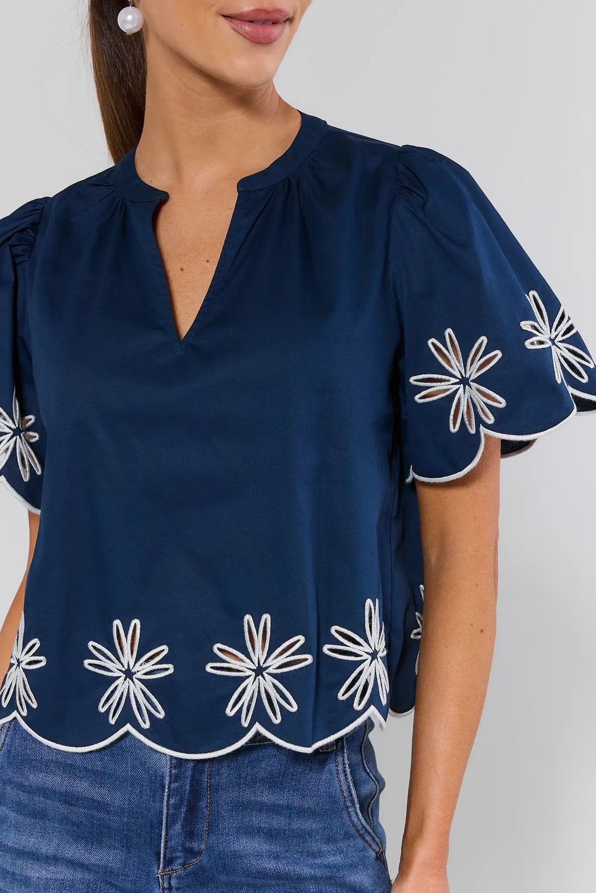 Navy embroidered blouse close-up showing white daisy eyelet trim on scalloped sleeves and hem - Detail View | Avara