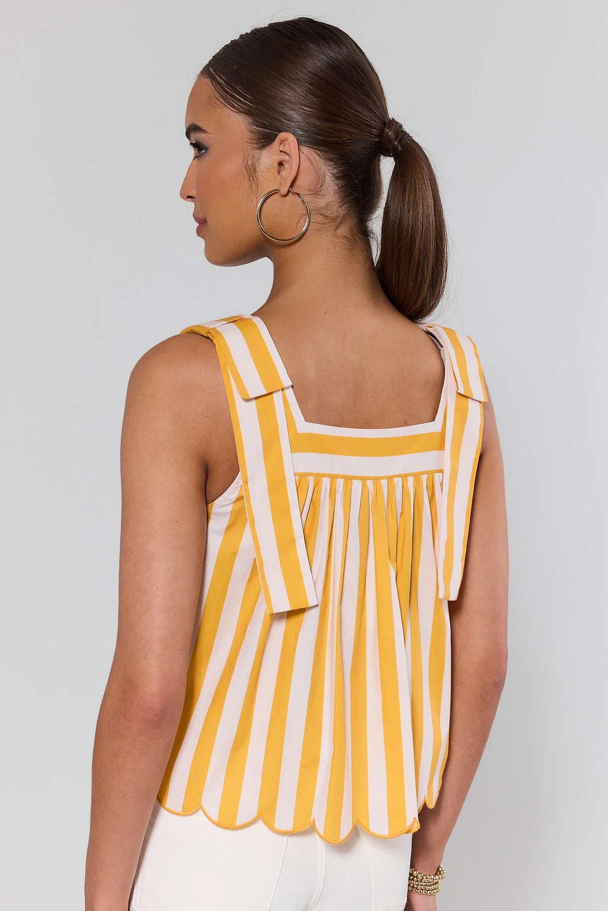 Back view of yellow striped tank top showing square back neckline, bow straps, and scalloped hem | Avara