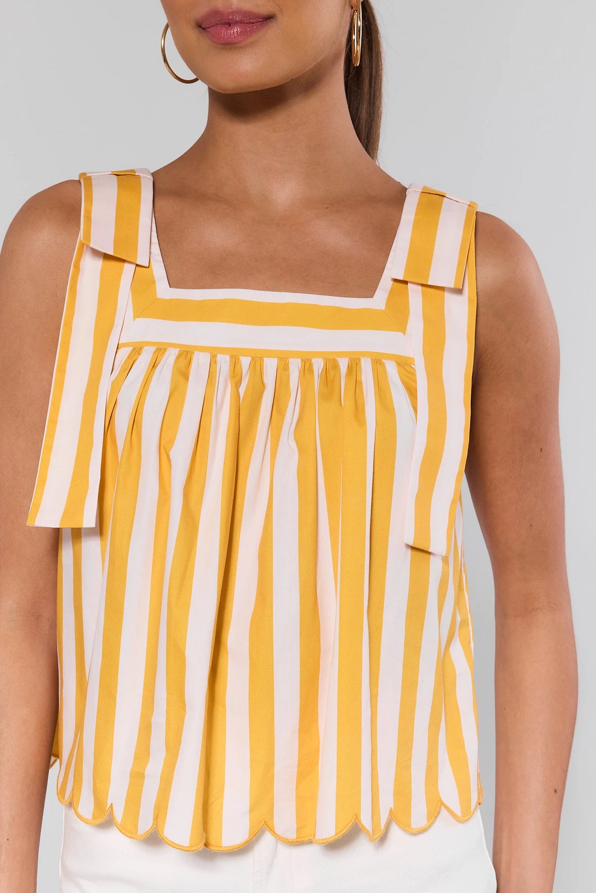 Close-up of yellow striped tank top showing square neckline, bow strap detail, and scalloped hem | Avara