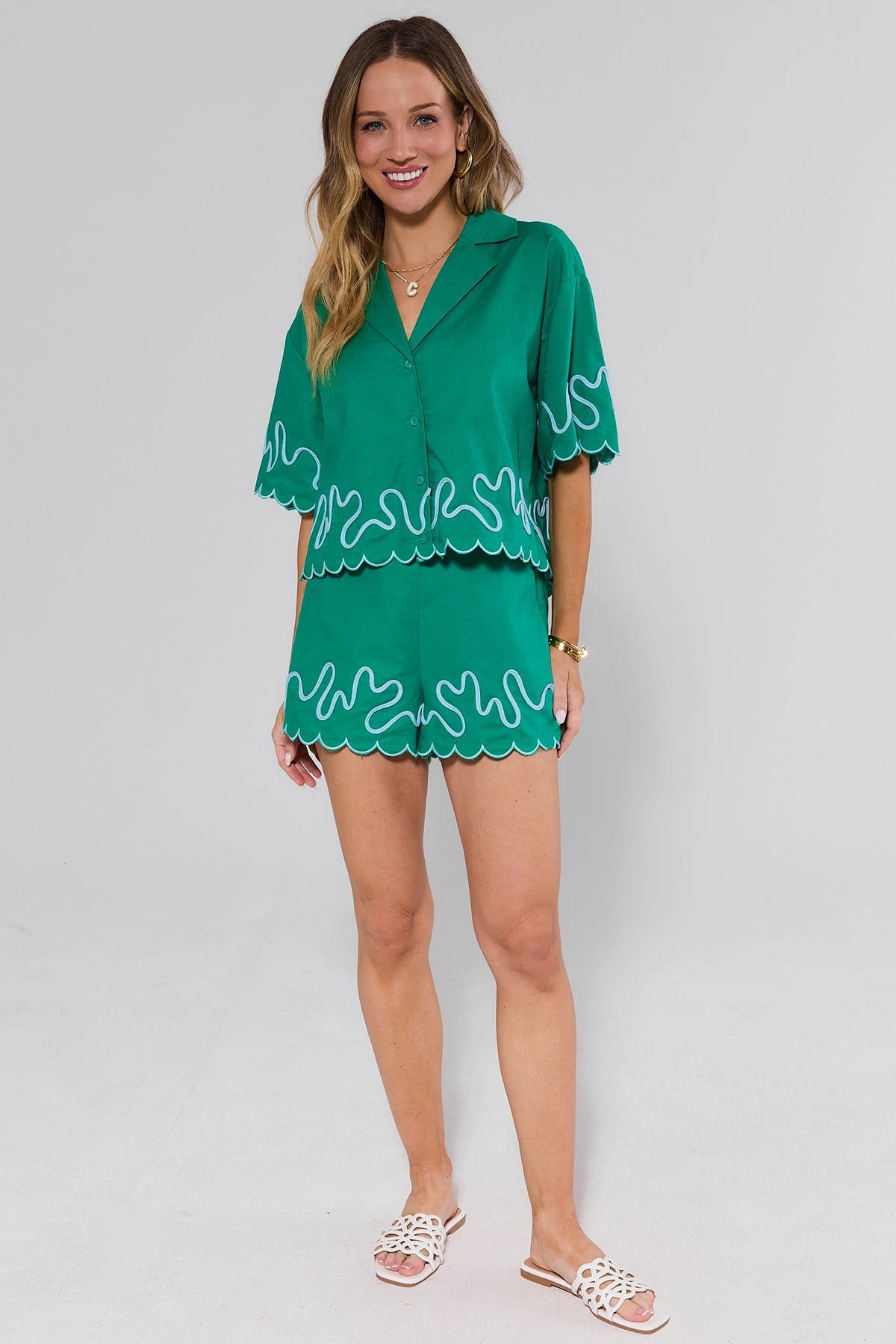 Woman wearing a green shorts and top with white lace details on a gray background