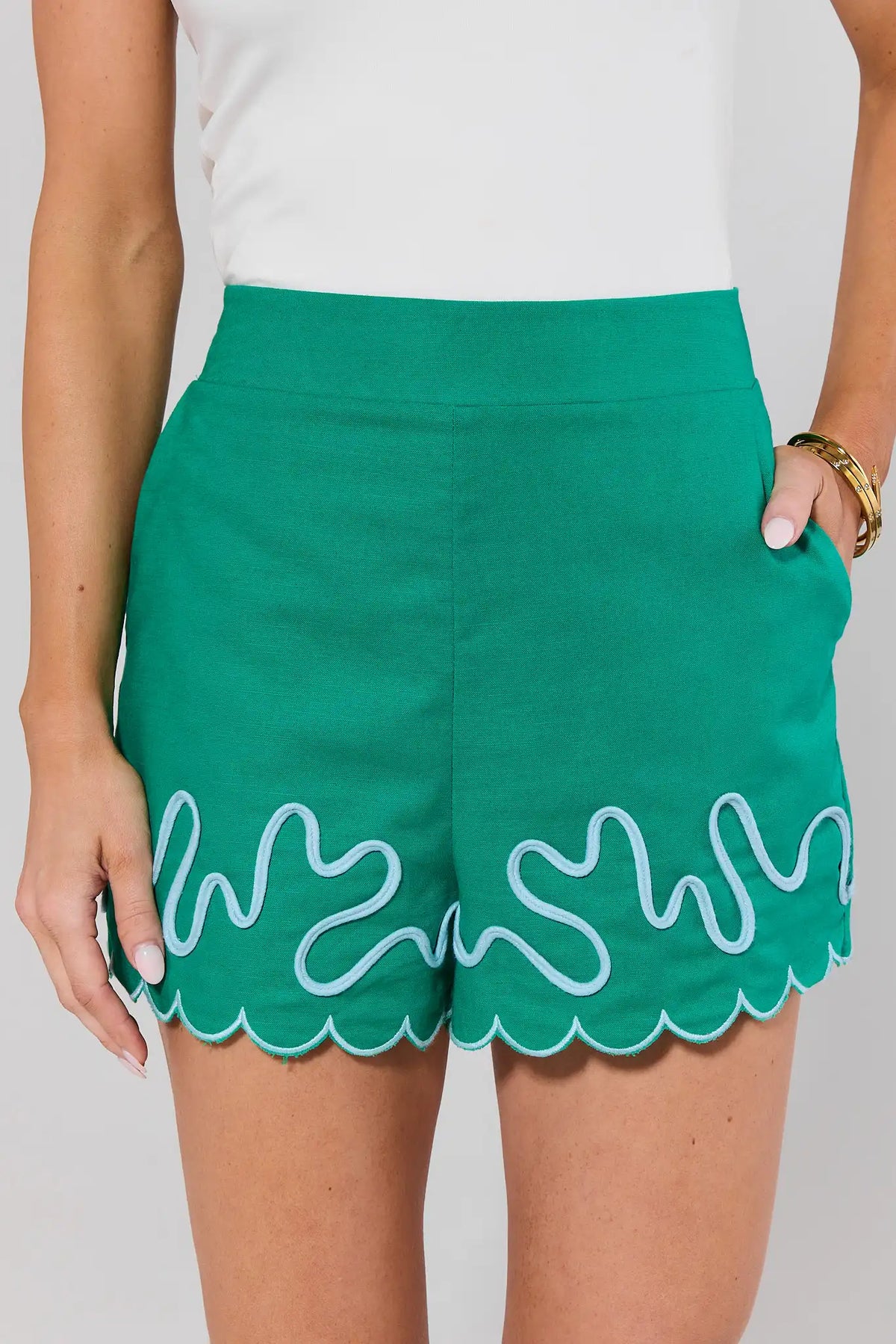 Green shorts with white scalloped hem on a plain background